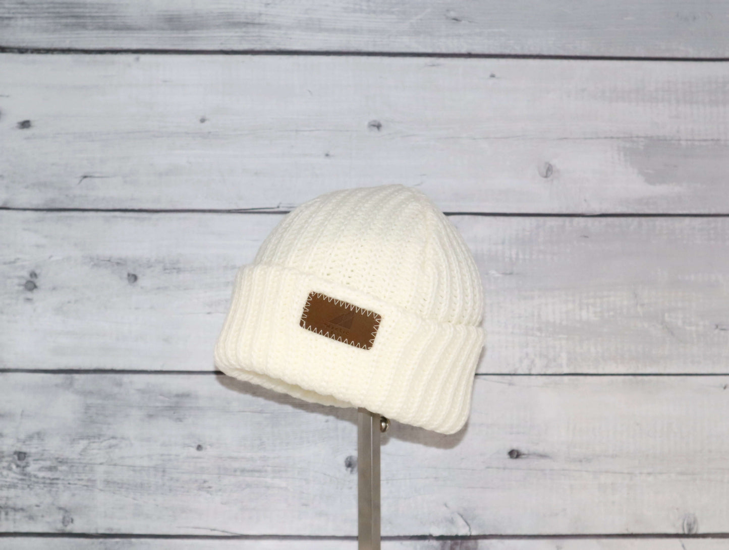 Toddler Acrylic Ribbed Cuff Hat – Soft, Stretchy & Made to Give displayed on a stand against a rustic wood background.