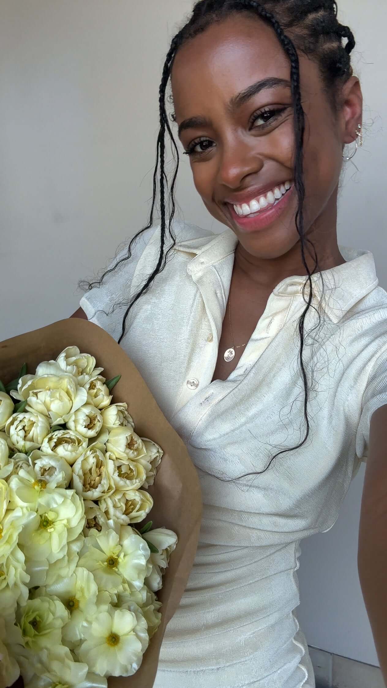 A smiling person wearing a light-colored outfit, holding a bouquet of white flowers.