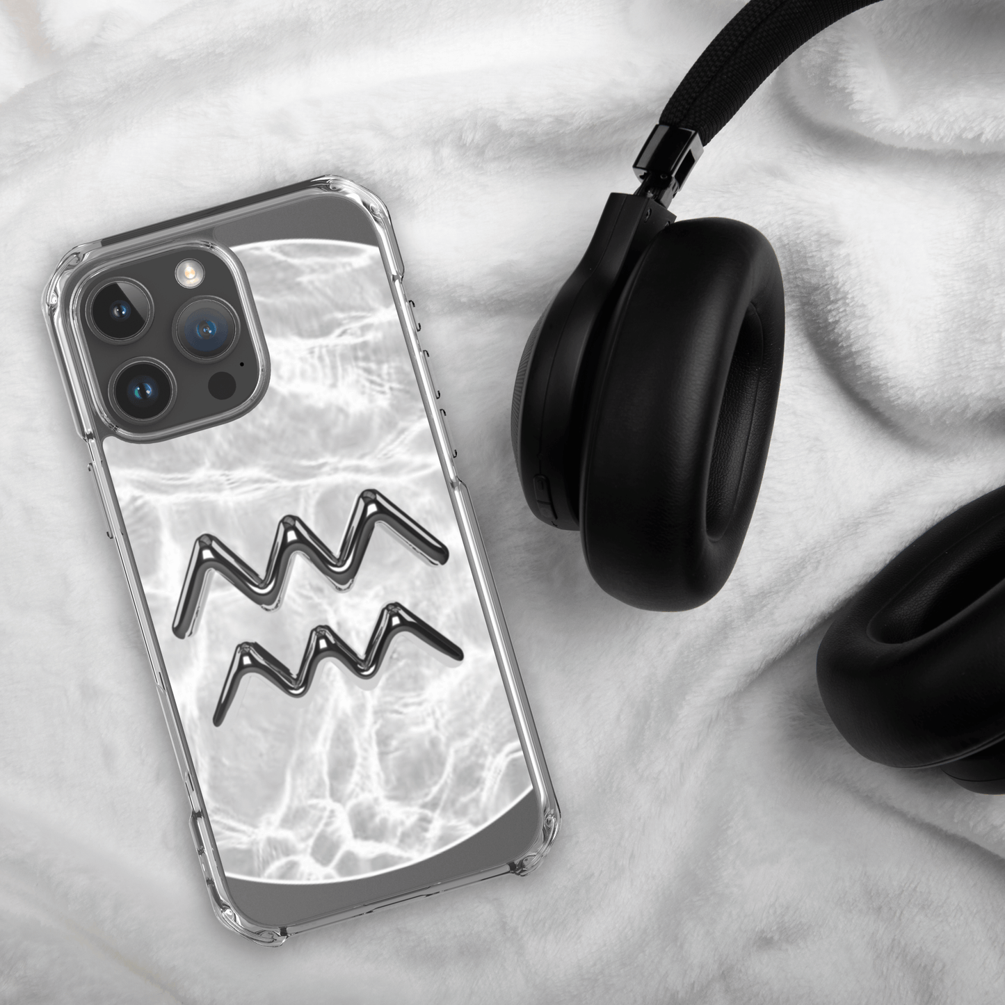 Zodiac Aquarius clear iPhone case with marble design next to black headphones on a soft fabric background.