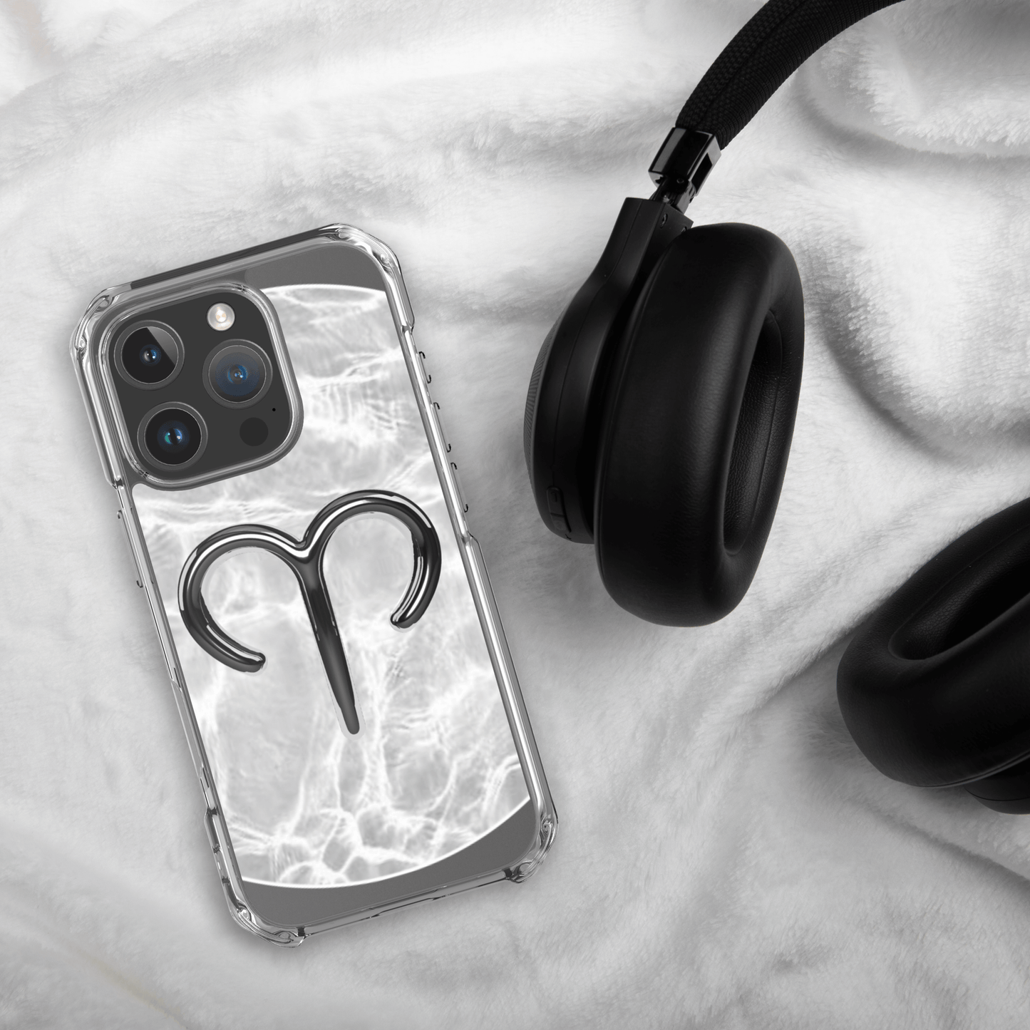 Zodiac Aries MagSafe clear iPhone case with metallic design on a soft surface next to black headphones.