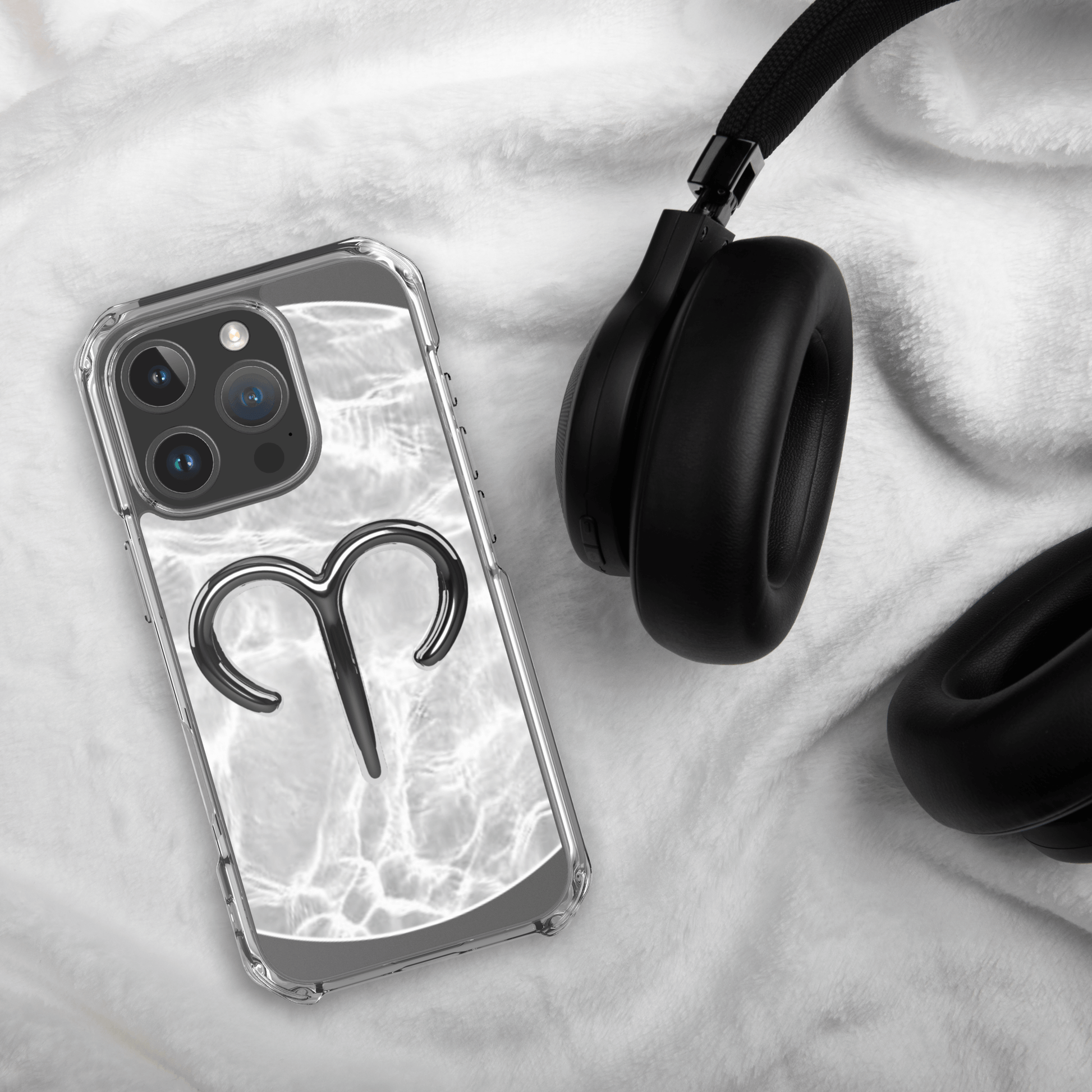 Zodiac Aries MagSafe clear iPhone case with metallic design on a soft surface next to black headphones.