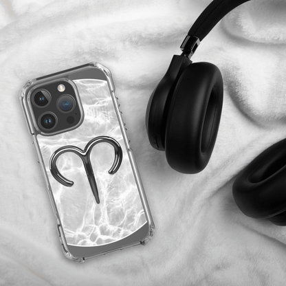 Zodiac Aries MagSafe clear iPhone case with metallic design on a soft surface next to black headphones.