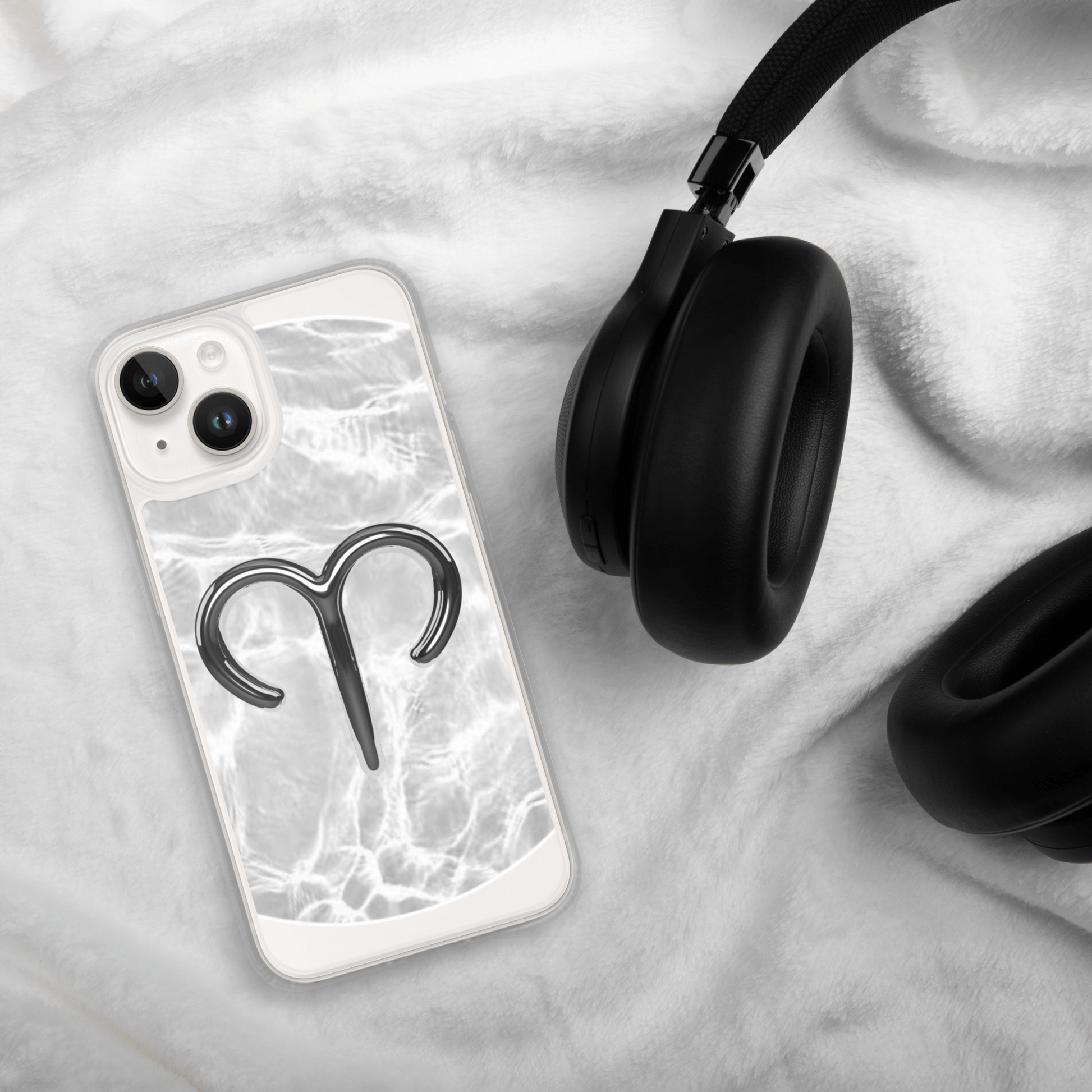 Zodiac Aries MagSafe clear iPhone case with metallic design on a cozy fabric, next to stylish headphones.