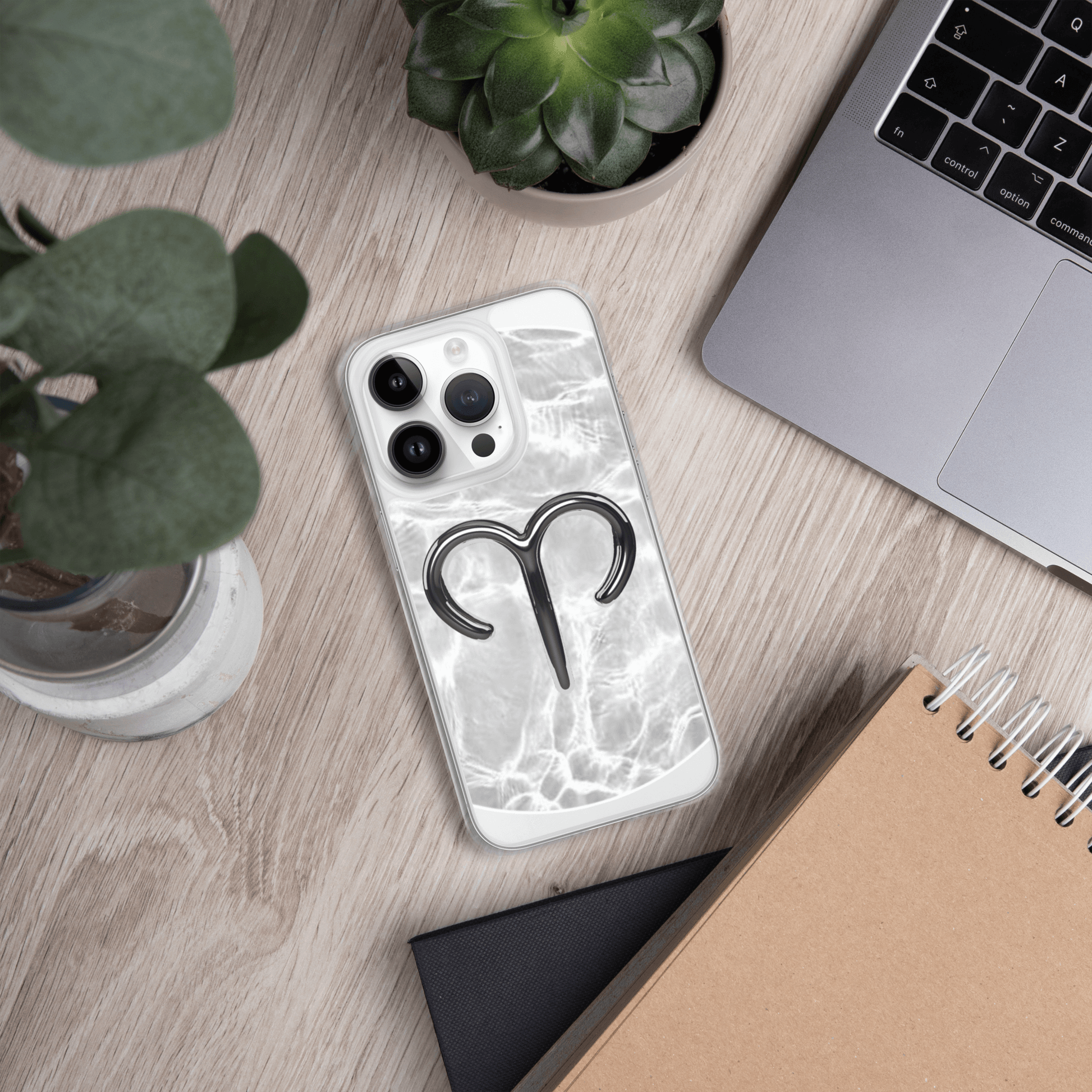 Zodiac Aries MagSafe clear iPhone case with marble metallic design on a desktop with plants and notebook.