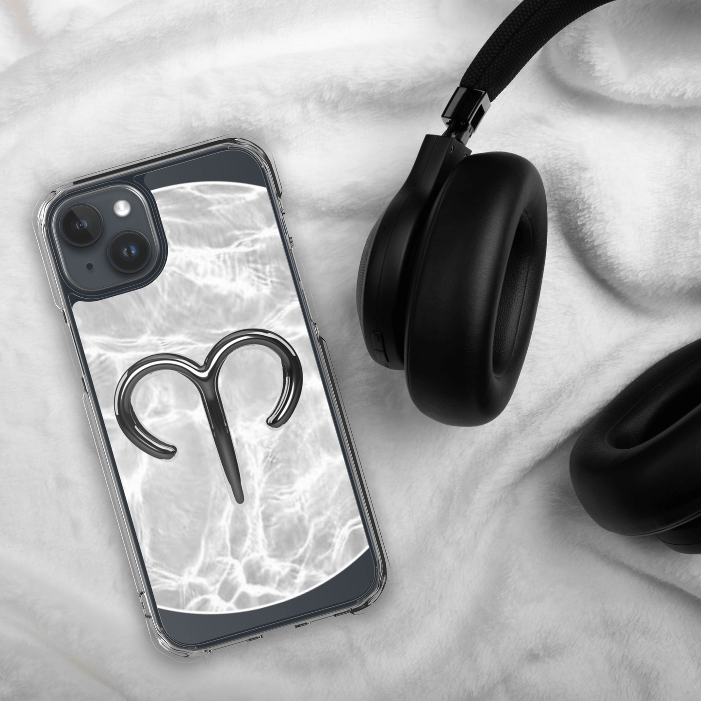 Zodiac Aries MagSafe clear iPhone case with marble design and metallic symbol next to black headphones