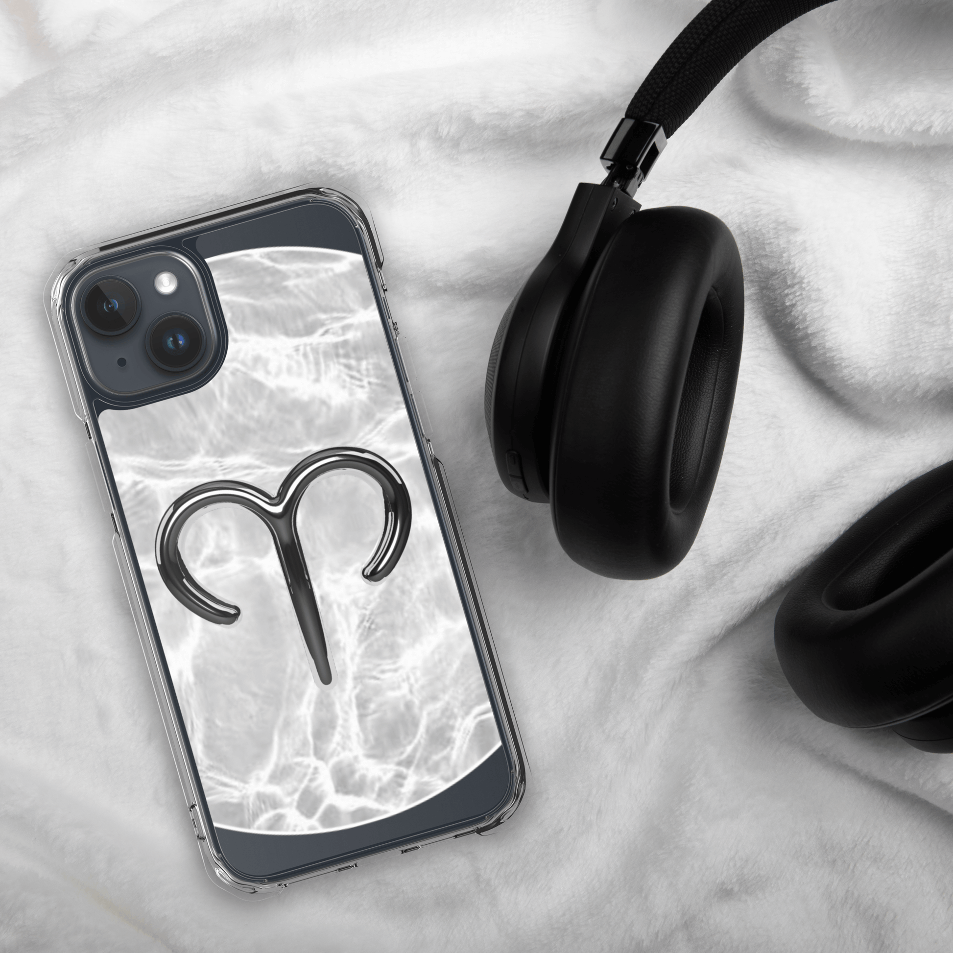 Zodiac Aries MagSafe clear iPhone case with marble design and metallic symbol next to black headphones