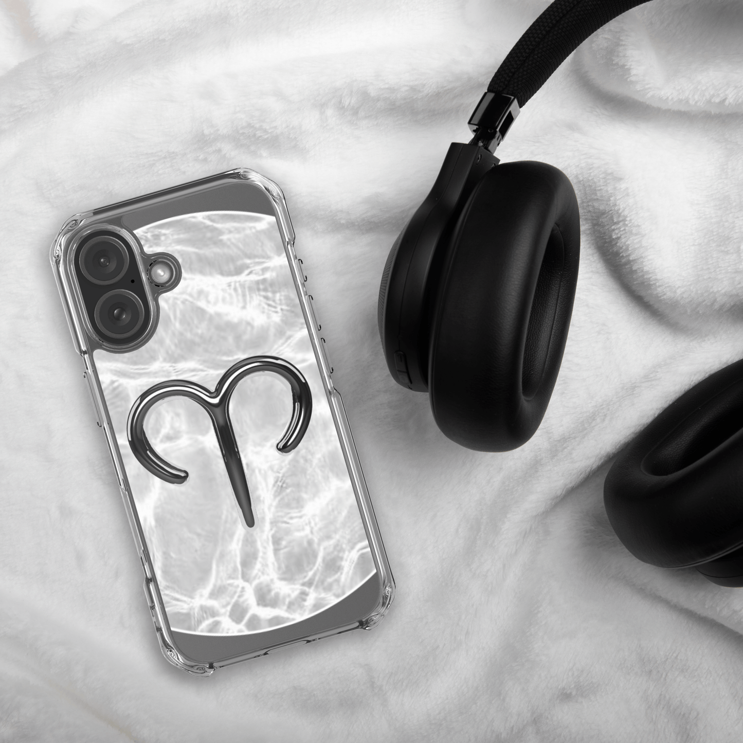 Zodiac Aries MagSafe clear iPhone case featuring a metallic design on a marble background, next to black headphones.