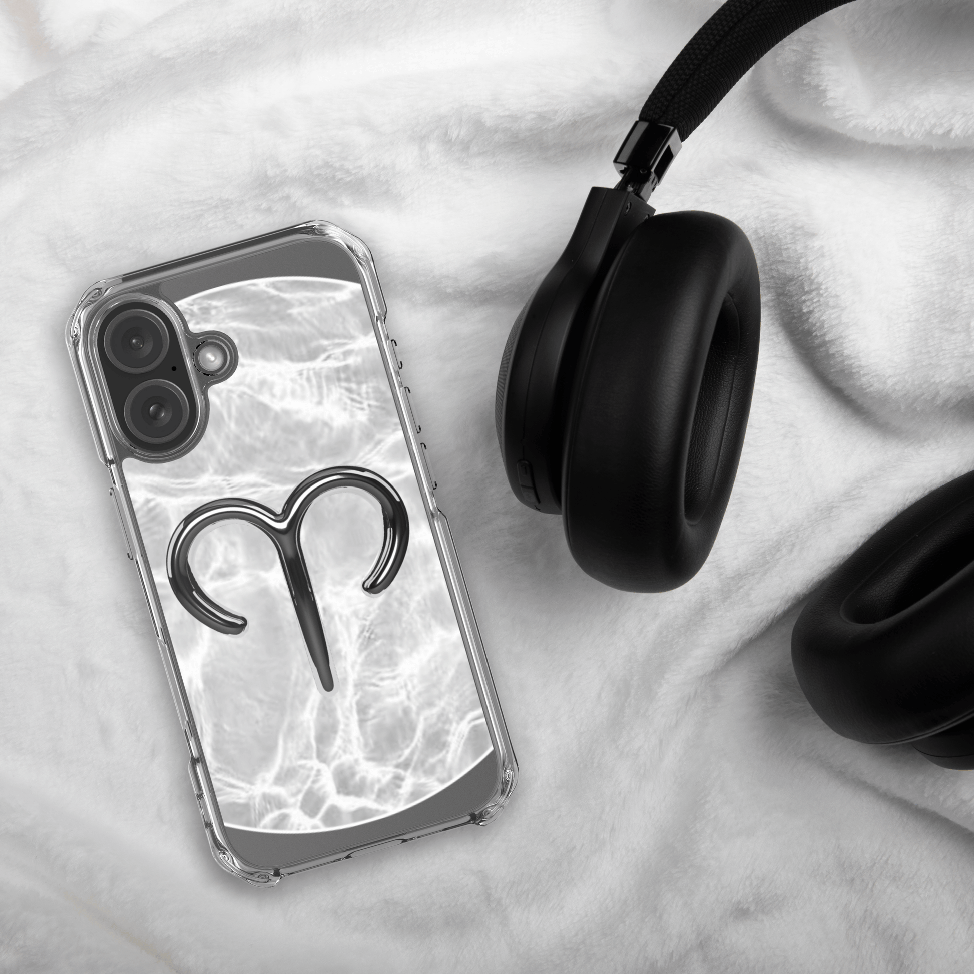 Zodiac Aries MagSafe clear iPhone case featuring a metallic design on a marble background, next to black headphones.