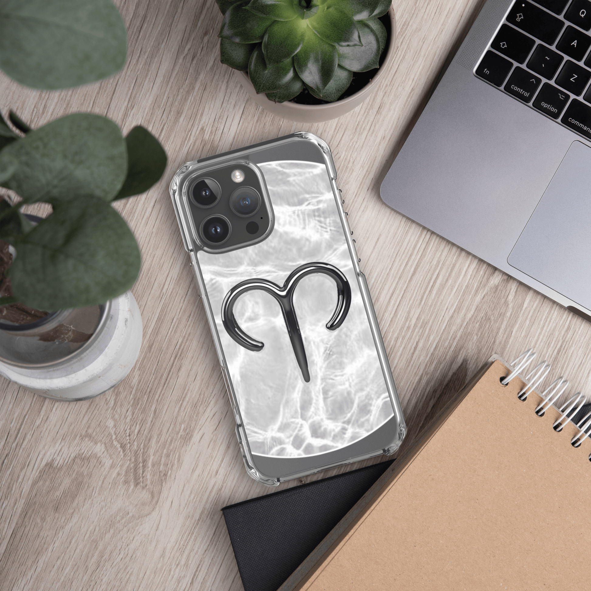 Zodiac Aries MagSafe clear iPhone case with marble metallic design on a desk with greenery and notebook.
