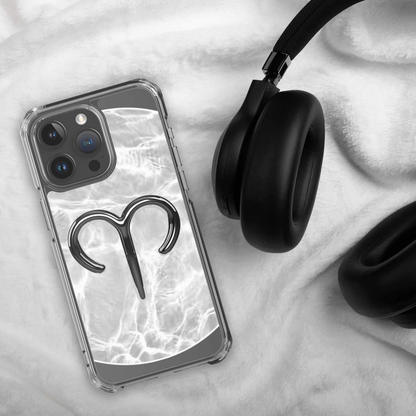 Zodiac Aries MagSafe clear iPhone case with metallic design next to headphones on soft fabric.