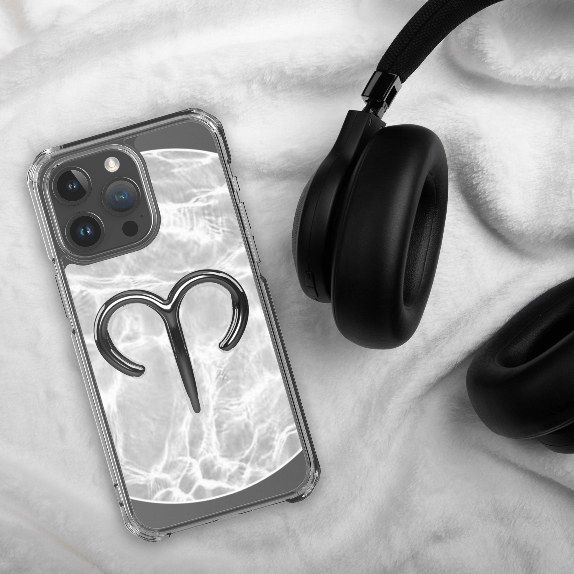 Zodiac Aries MagSafe clear iPhone case with metallic design next to headphones on soft fabric.