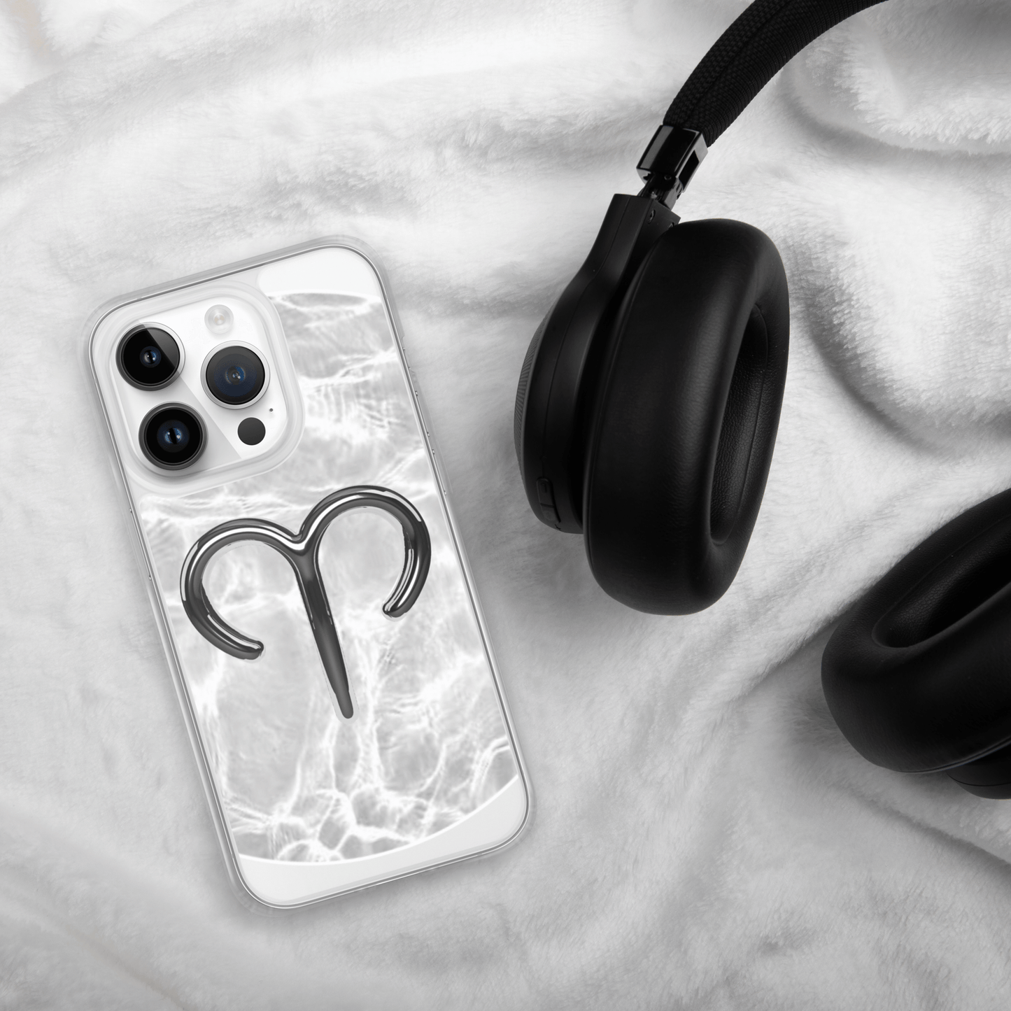 Zodiac Aries MagSafe clear iPhone case with marble design next to black headphones on soft white blanket.