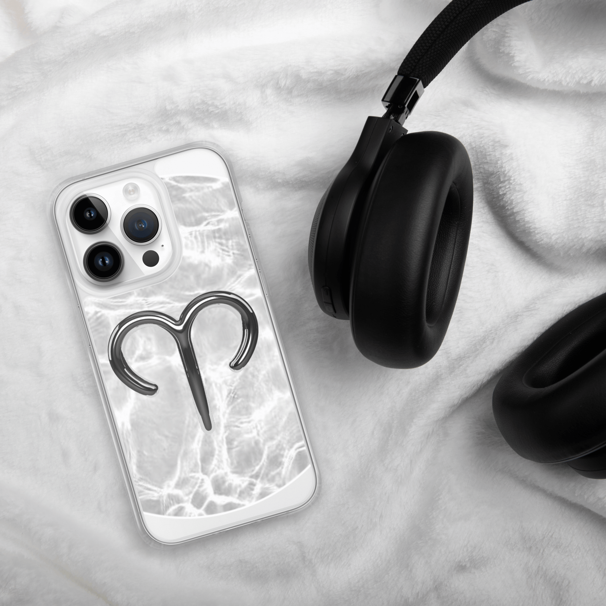 Zodiac Aries MagSafe clear iPhone case with marble design next to black headphones on soft white blanket.