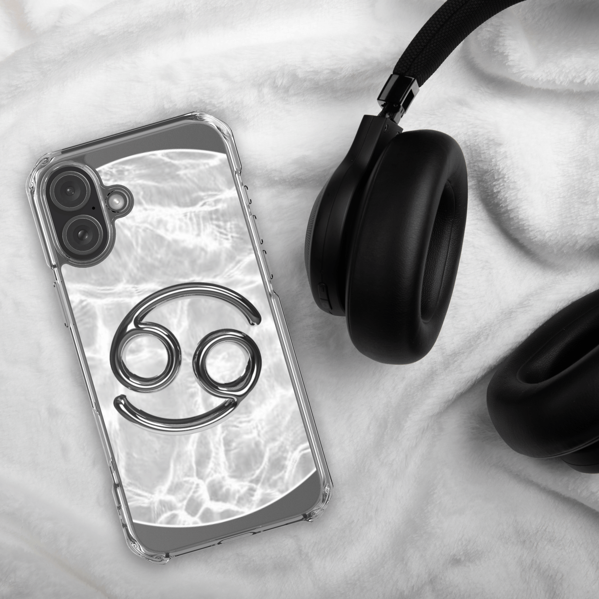 Zodiac Cancer MagSafe clear iPhone case with metallic design on a plush surface next to black headphones.