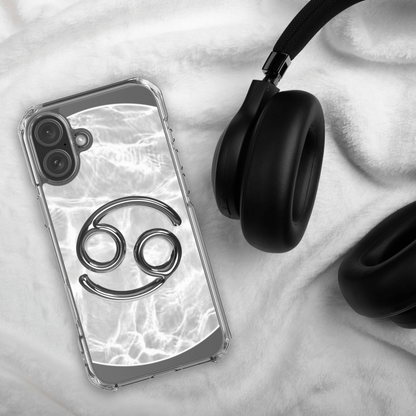 Zodiac Cancer MagSafe clear iPhone case with metallic design on a plush surface next to black headphones.