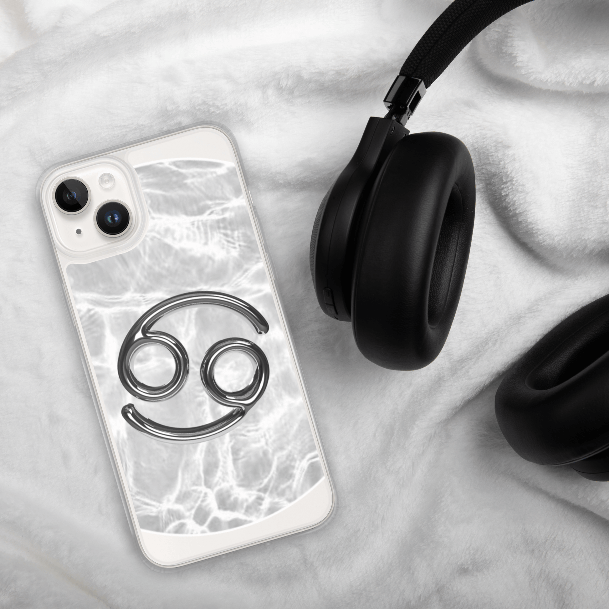 Zodiac Cancer MagSafe clear iPhone case with metallic design on soft backdrop next to black headphones.