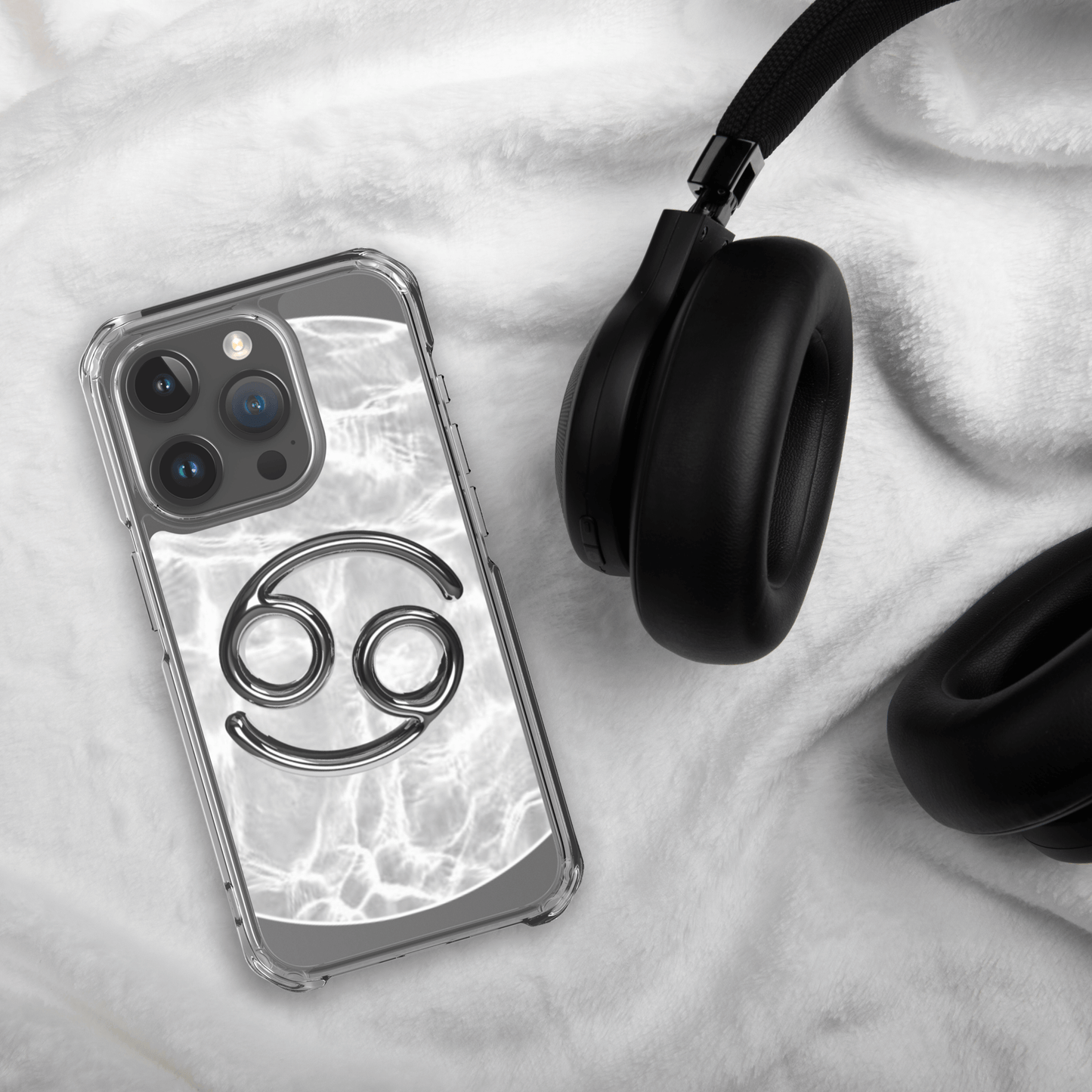 Zodiac Cancer Magsafe clear iPhone case with metallic design on marble background next to black headphones.