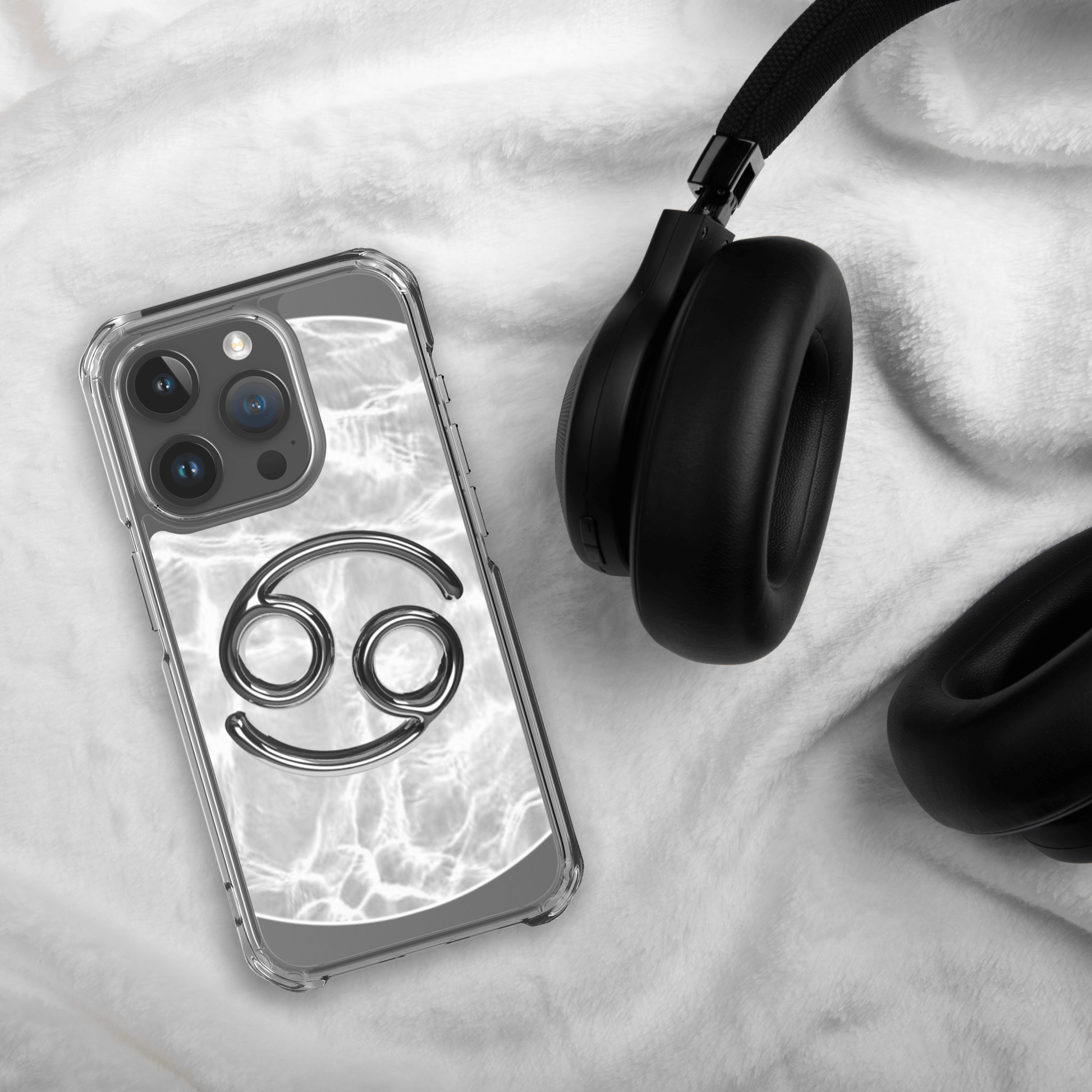 Zodiac Cancer Magsafe clear iPhone case with metallic design on marble background next to black headphones.