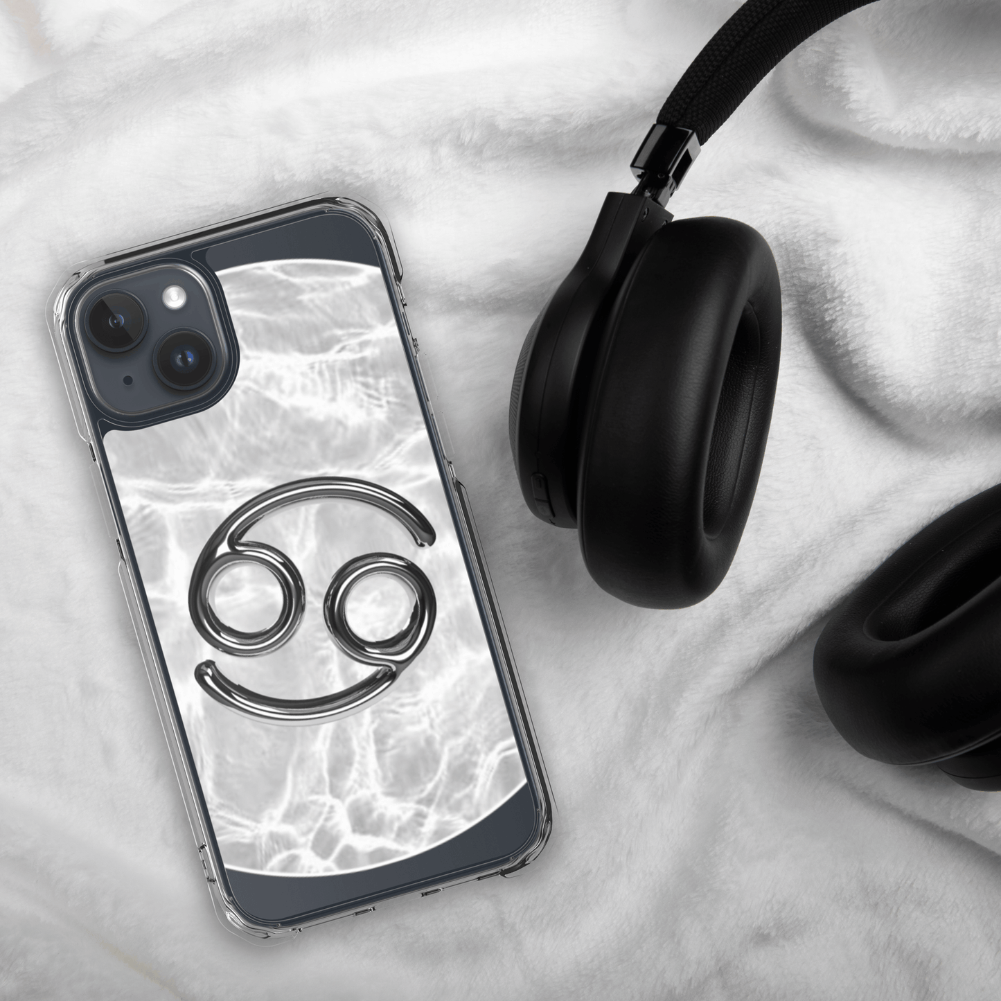 Zodiac Cancer MagSafe clear iPhone case with metallic design atop a marble background next to black headphones.