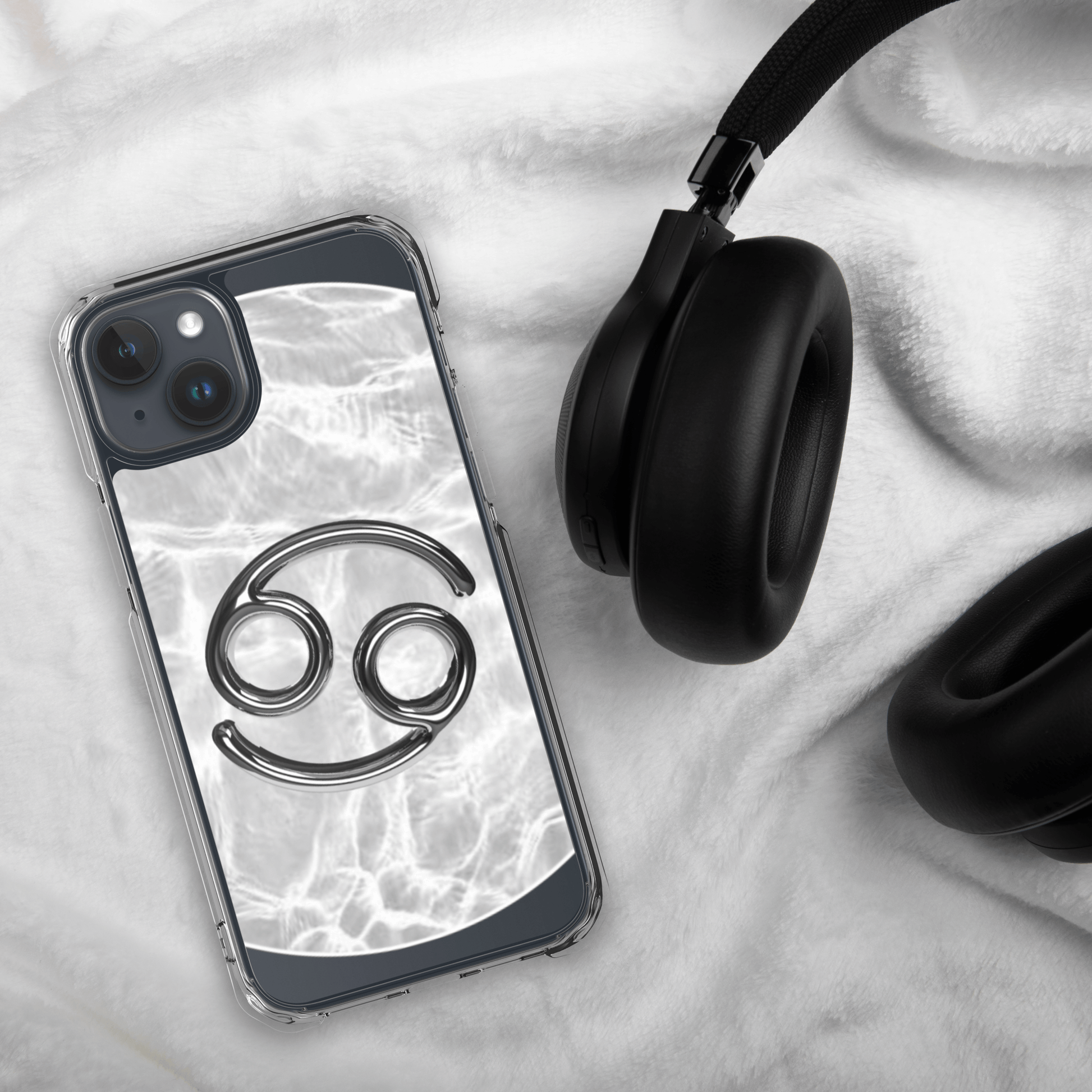 Zodiac Cancer MagSafe clear iPhone case with metallic design atop a marble background next to black headphones.
