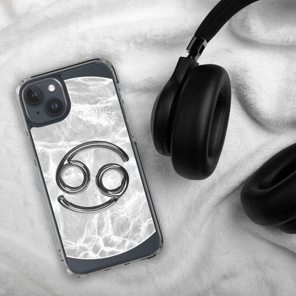 Zodiac Cancer MagSafe clear iPhone case with metallic design atop a marble background next to black headphones.
