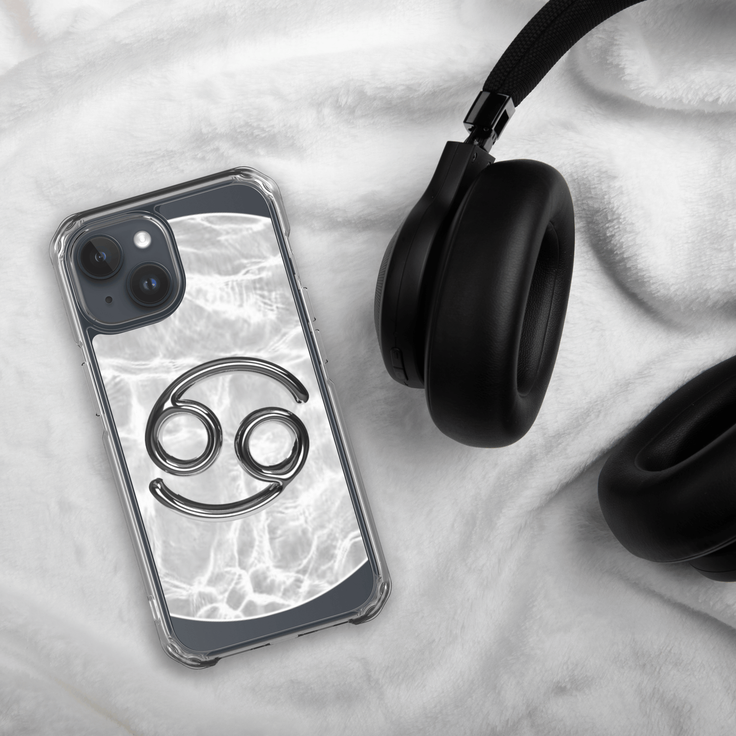 Zodiac Cancer Magsafe clear iPhone case with metallic design, marble background, beside black headphones.