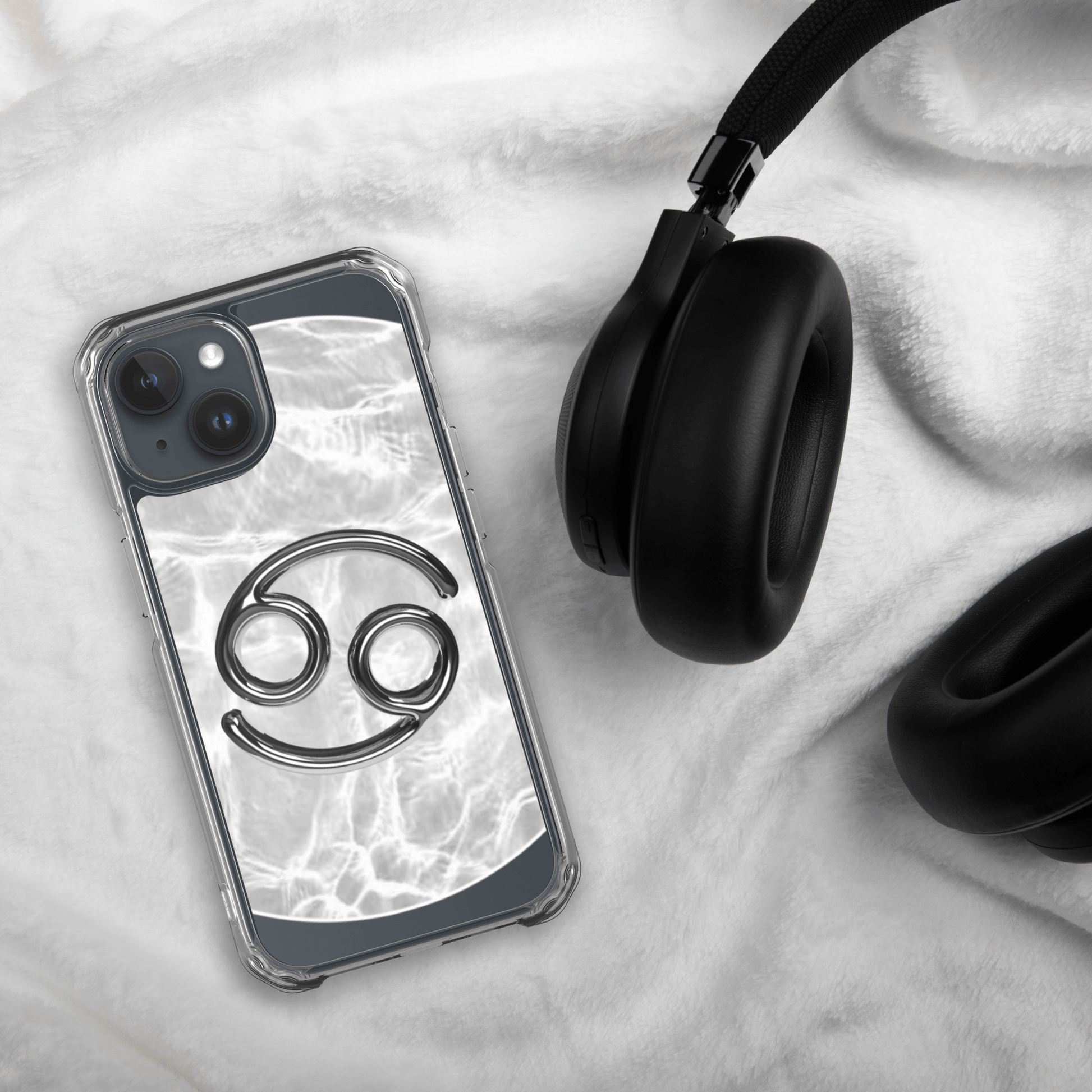 Zodiac Cancer Magsafe clear iPhone case with metallic design, marble background, beside black headphones.