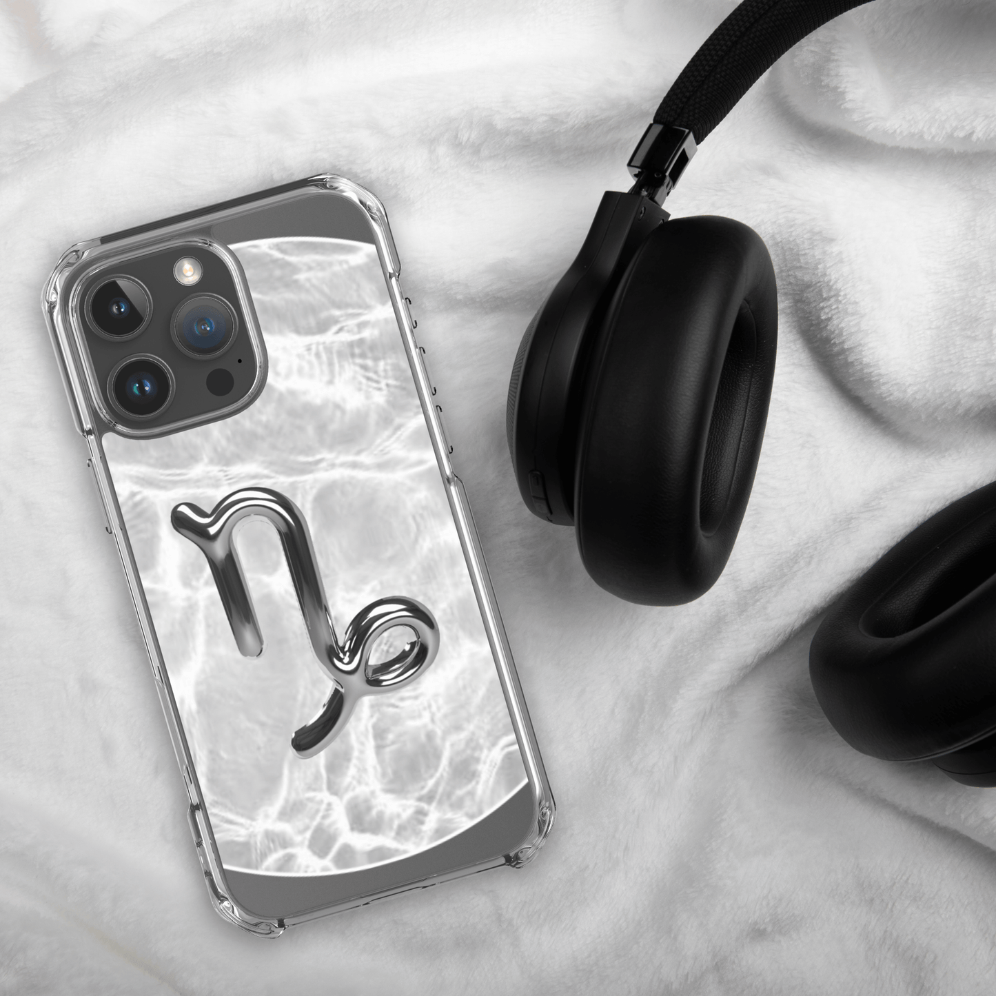 Zodiac Capricorn MagSafe clear iPhone case with metallic design on marble, next to black headphones.