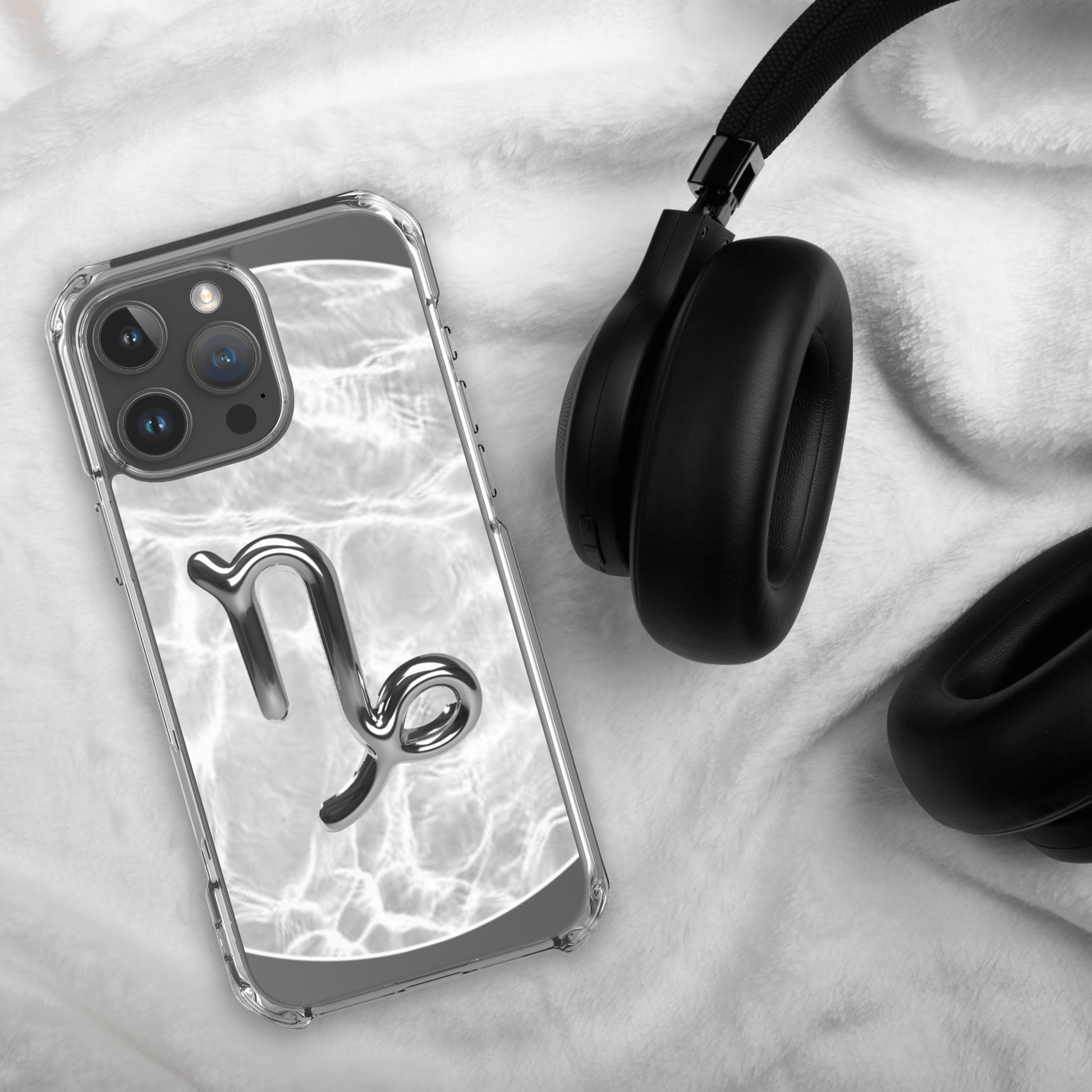 Zodiac Capricorn MagSafe clear iPhone case with metallic design on marble, next to black headphones.