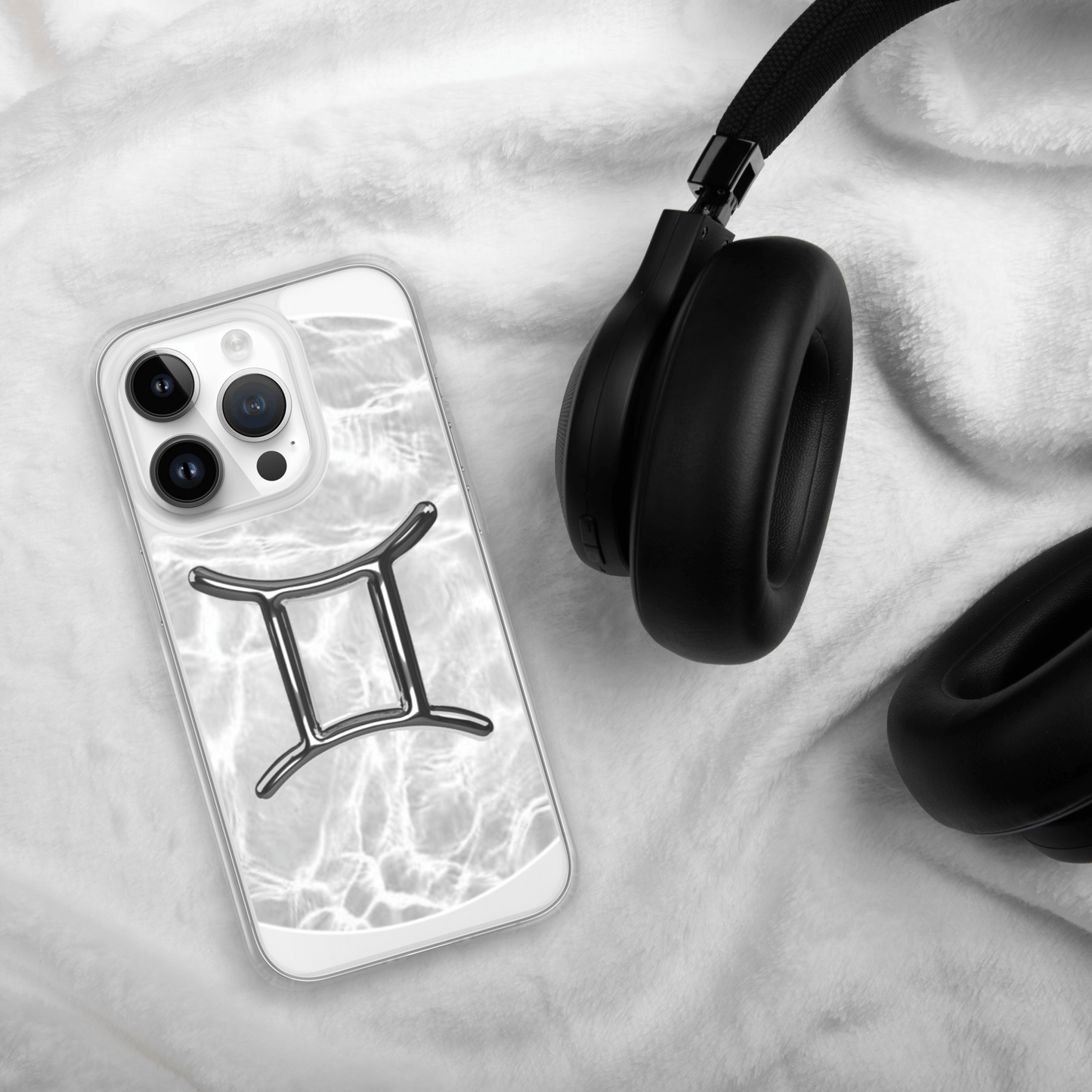 Gemini Magsafe clear iPhone case with marble design next to black headphones on soft fabric.