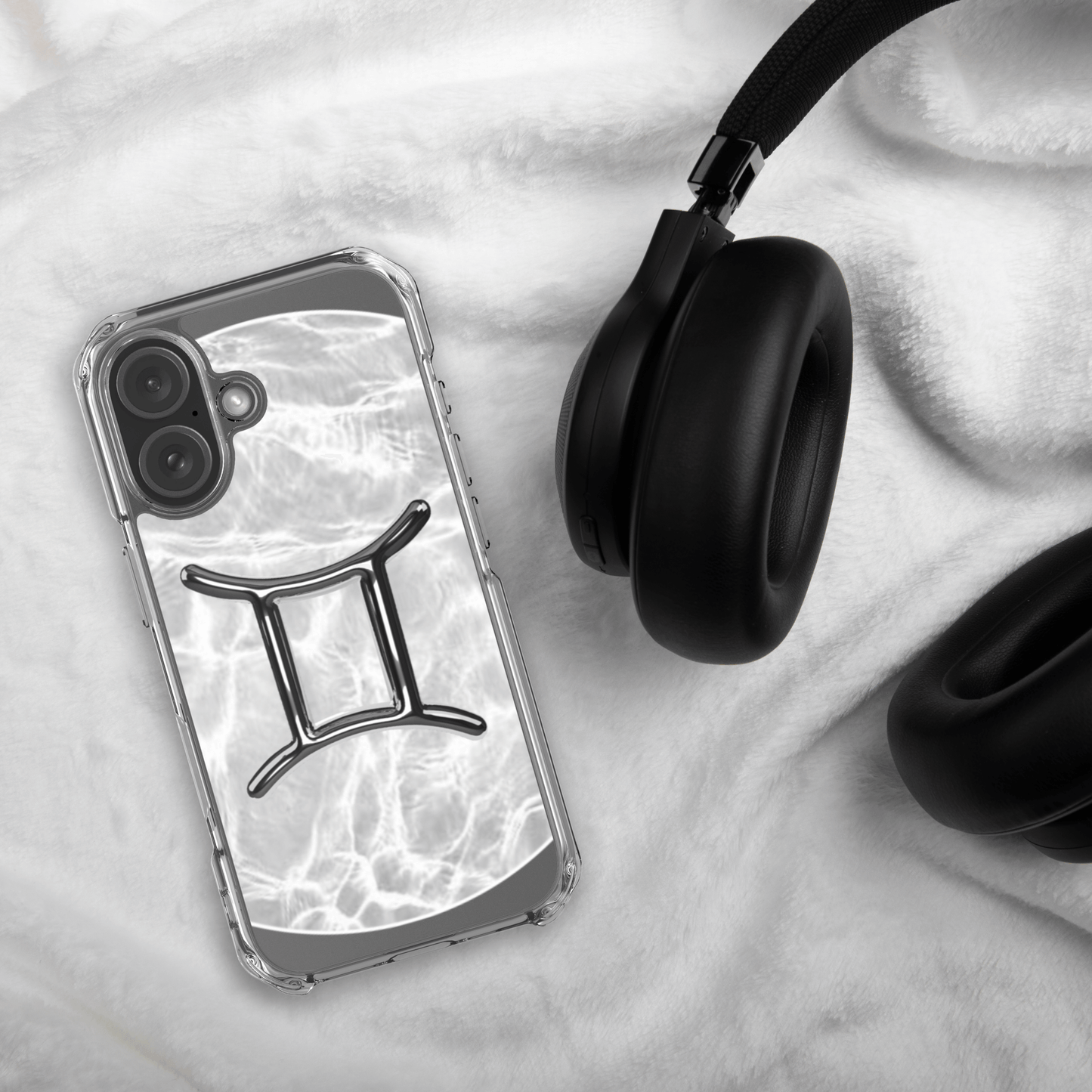 Zodiac Gemini MagSafe clear iPhone case in marble design next to black headphones on soft fabric background.