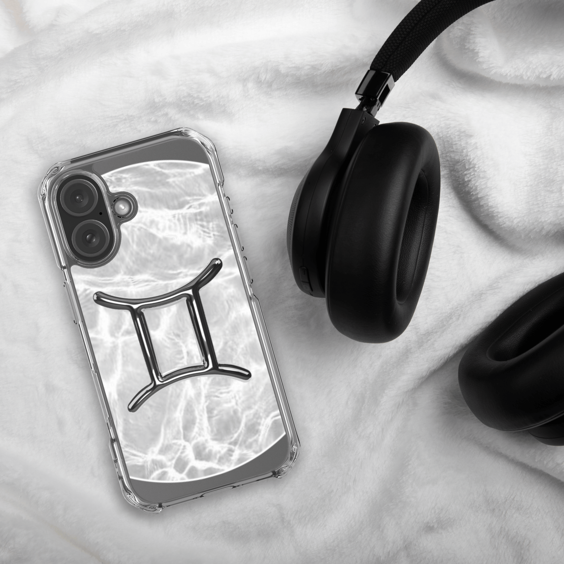 Zodiac Gemini MagSafe clear iPhone case in marble design next to black headphones on soft fabric background.
