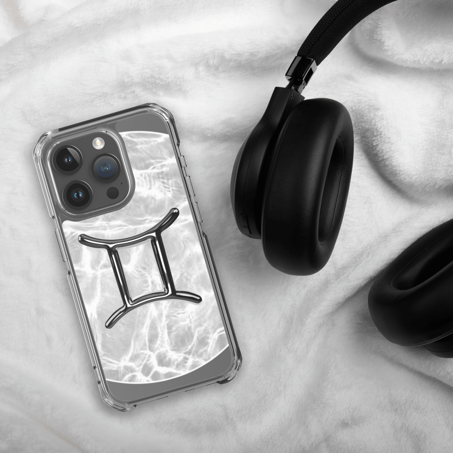 Zodiac Gemini MagSafe clear iPhone case with marble metallic design beside black headphones on soft surface.