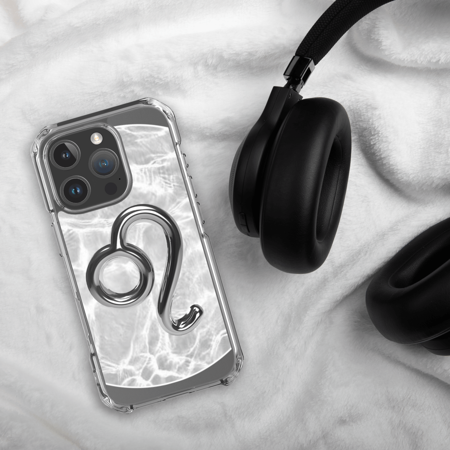 Zodiac Leo Magsafe clear iPhone case with metallic design on soft blanket next to black headphones.