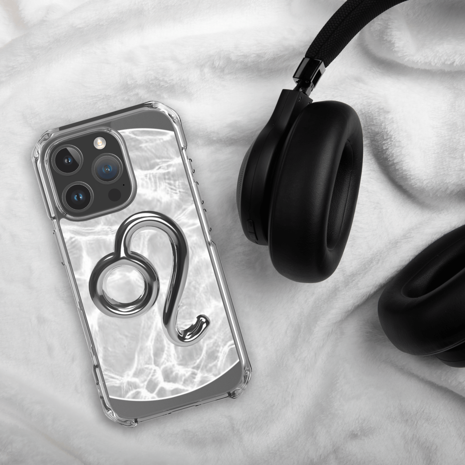 Zodiac Leo Magsafe clear iPhone case with metallic design on soft blanket next to black headphones.