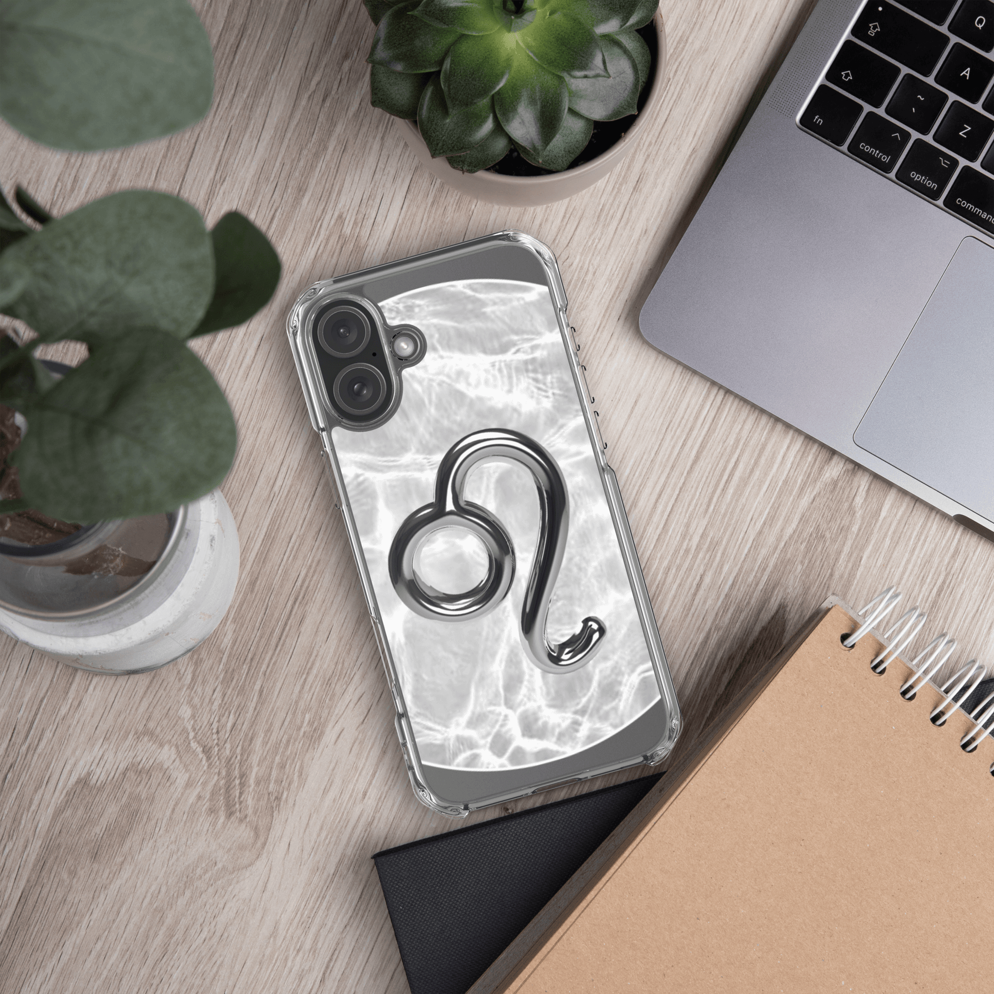 Zodiac Leo Magsafe clear iPhone case with metallic design on a wooden desk with plants and a laptop.