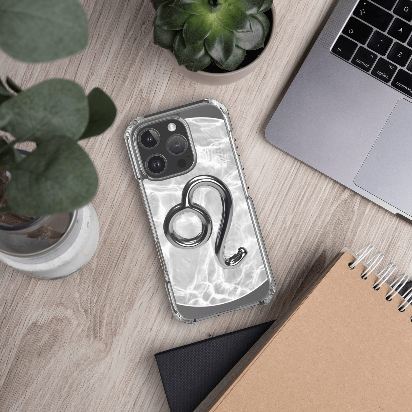 Zodiac Leo Magsafe clear iPhone case with metallic design on wood desk with plants and laptop.