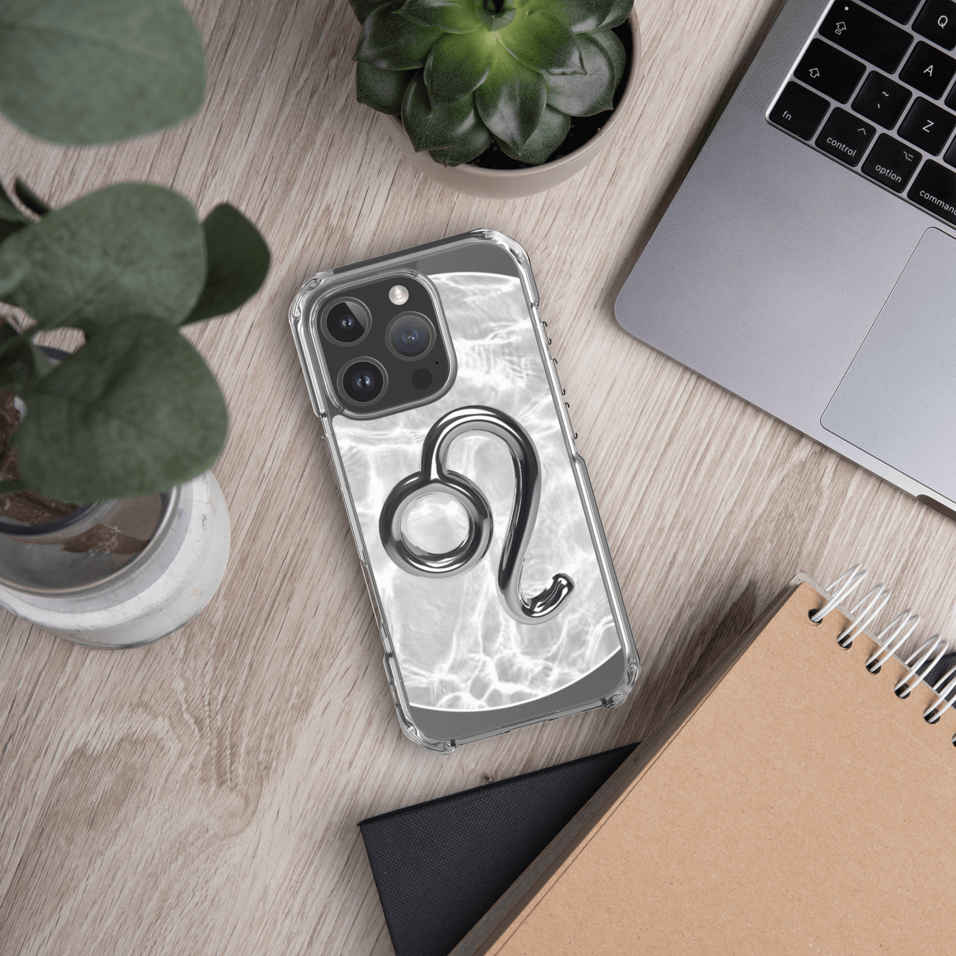 Zodiac Leo Magsafe clear iPhone case with metallic design on wood desk with plants and laptop.