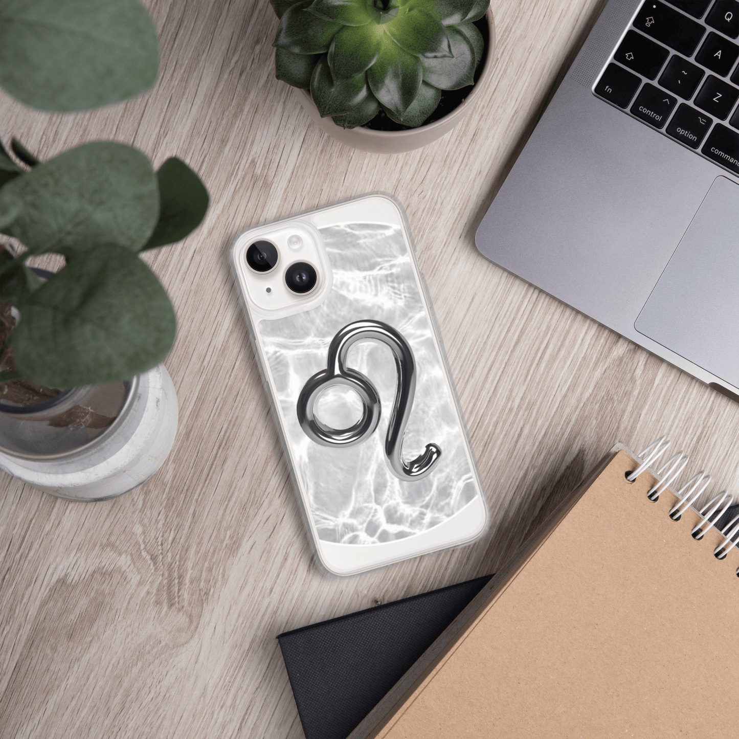 Zodiac Leo MagSafe clear iPhone case with metallic design on a marble background, surrounded by plants and a laptop.
