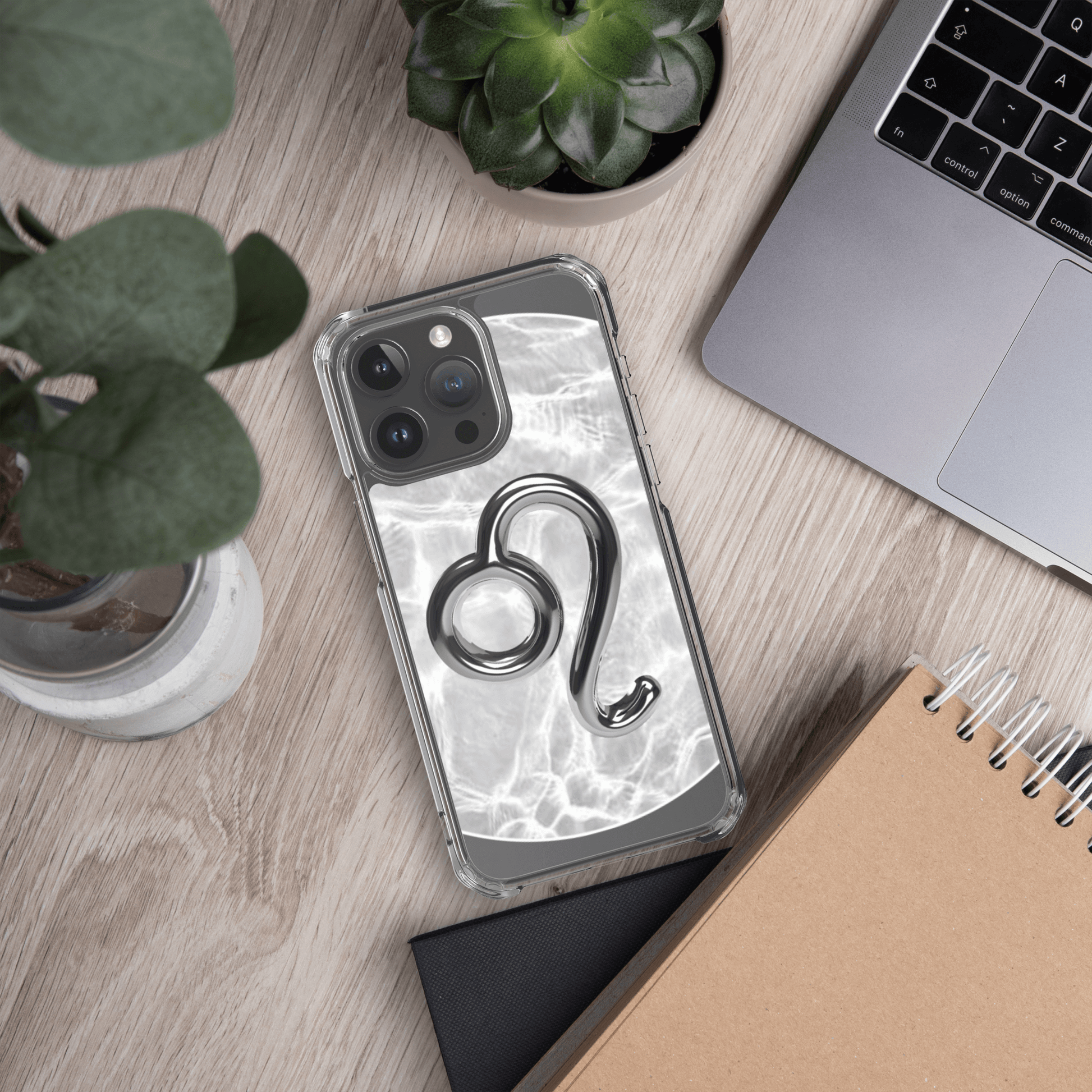 Zodiac Leo Magsafe clear iPhone case with marble metallic design on a wooden desk with plants and laptop.