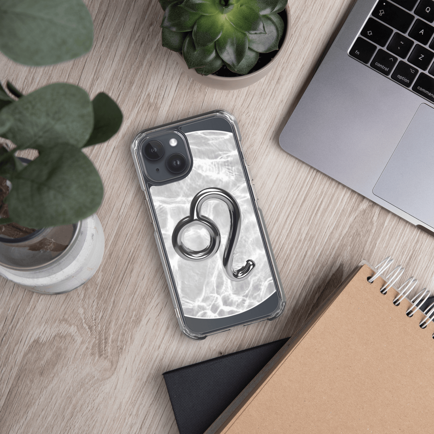 Clear iPhone case with Zodiac Leo design on a marble background, placed on a desk with plants and a notebook.