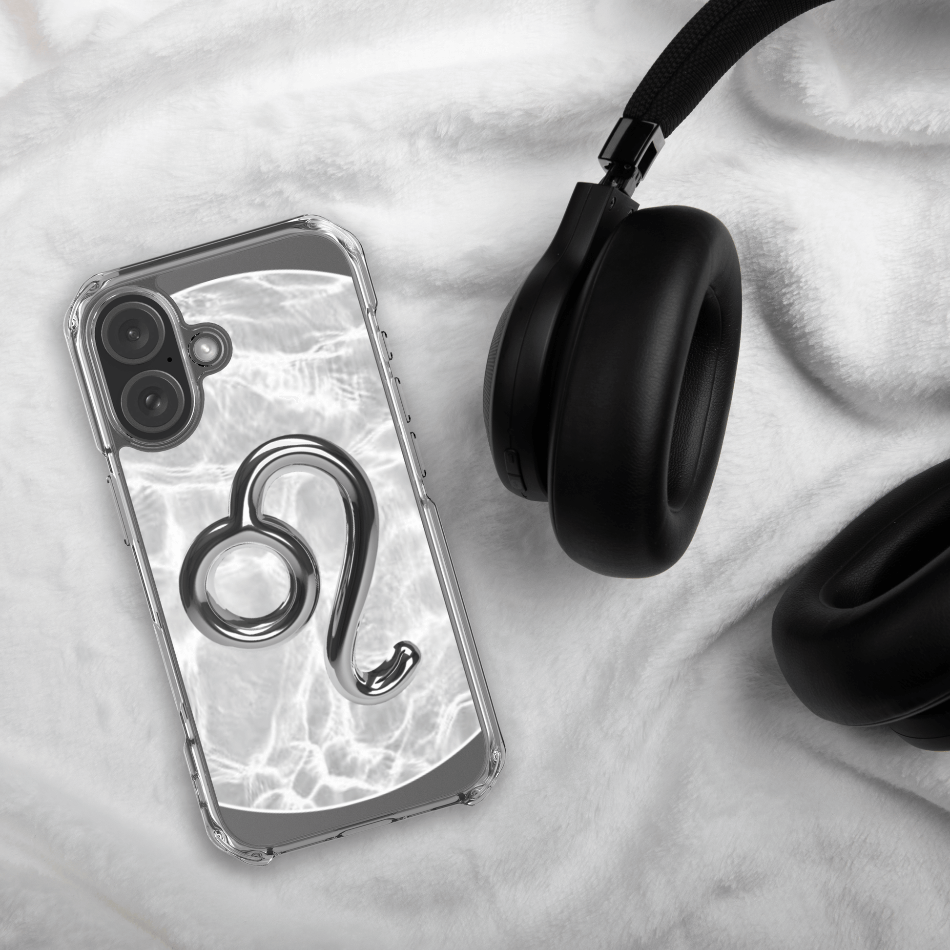 Zodiac Leo Magsafe clear iPhone case with metallic design on a soft surface beside black headphones.
