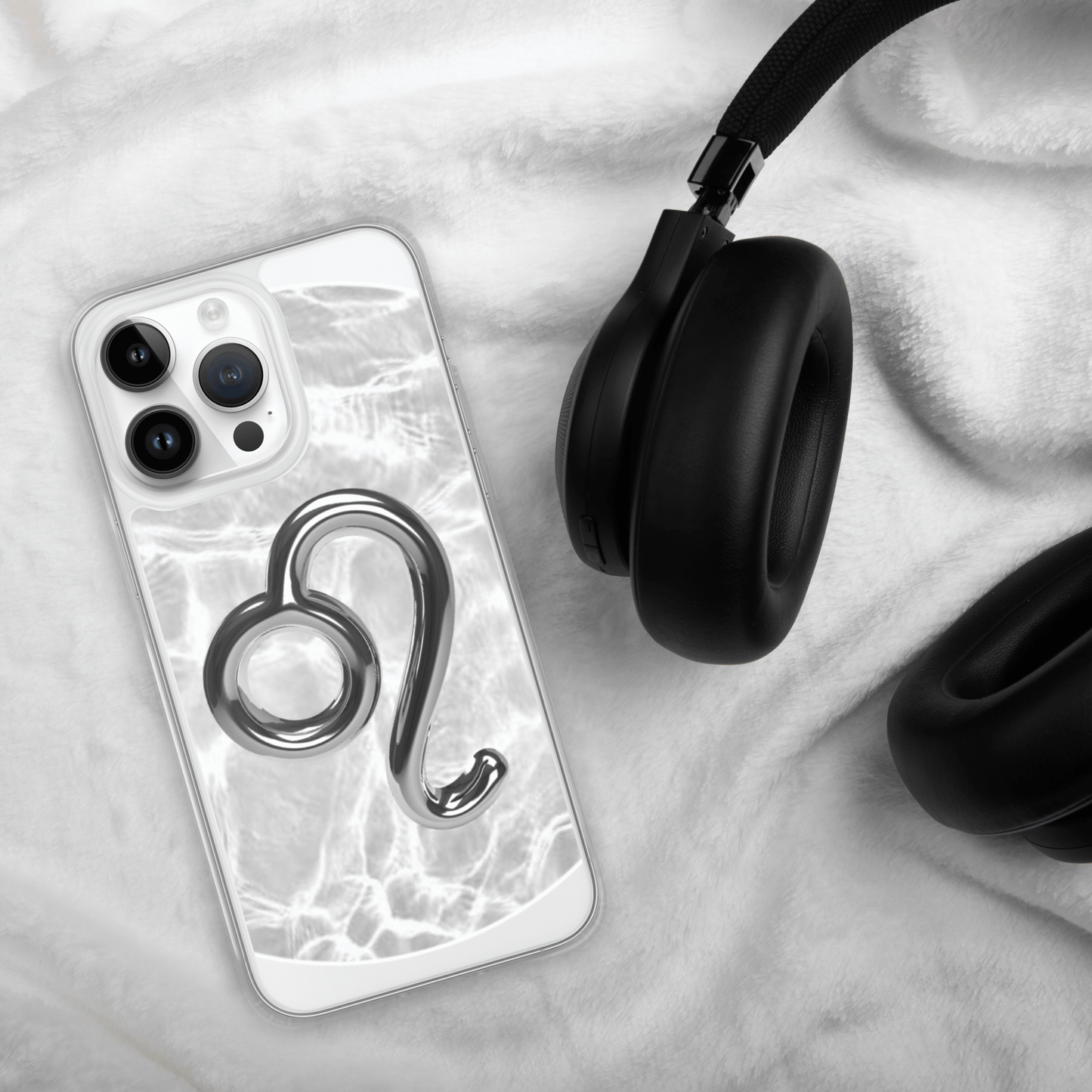 Zodiac Leo Magsafe iPhone case with metallic design on a soft white surface next to black headphones.