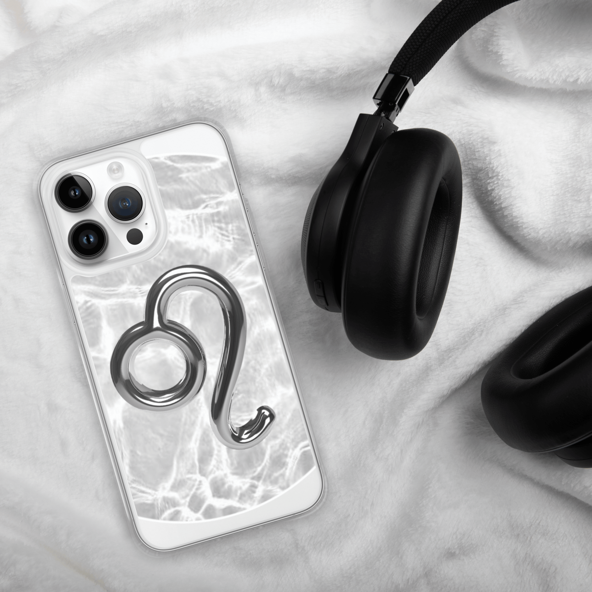 Zodiac Leo Magsafe iPhone case with metallic design on a soft white surface next to black headphones.