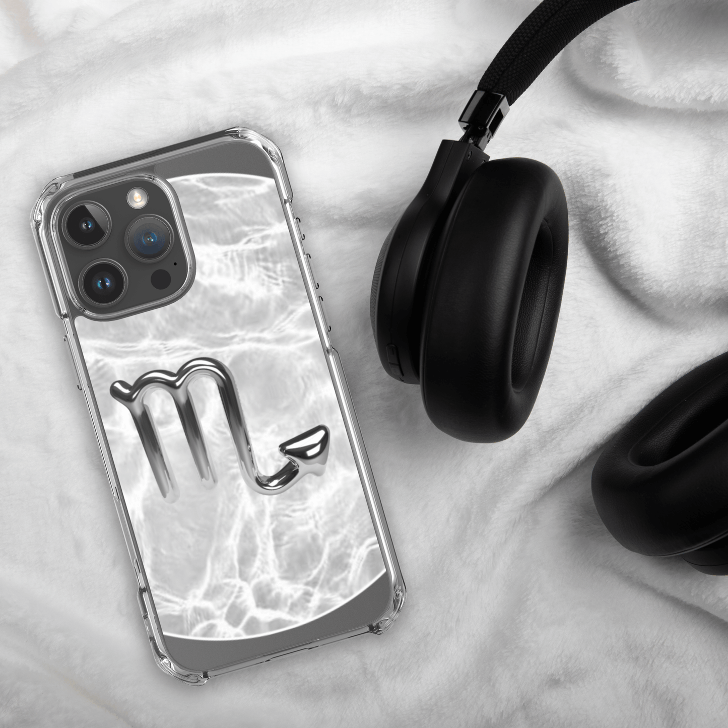 Zodiac Scorpio Magsafe clear iPhone case with metallic design, resting beside black headphones on a white cloth.