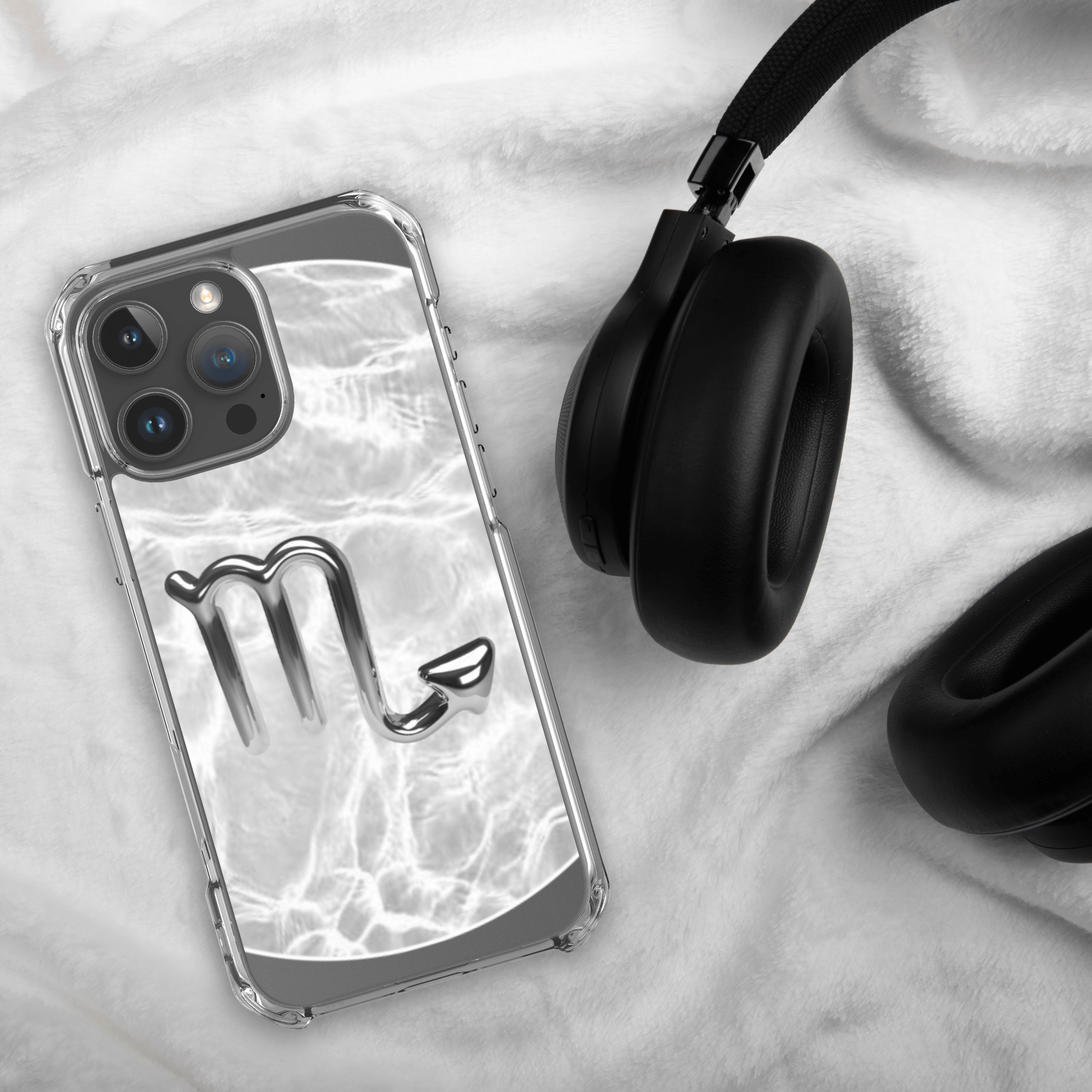 Zodiac Scorpio Magsafe clear iPhone case with metallic design, resting beside black headphones on a white cloth.