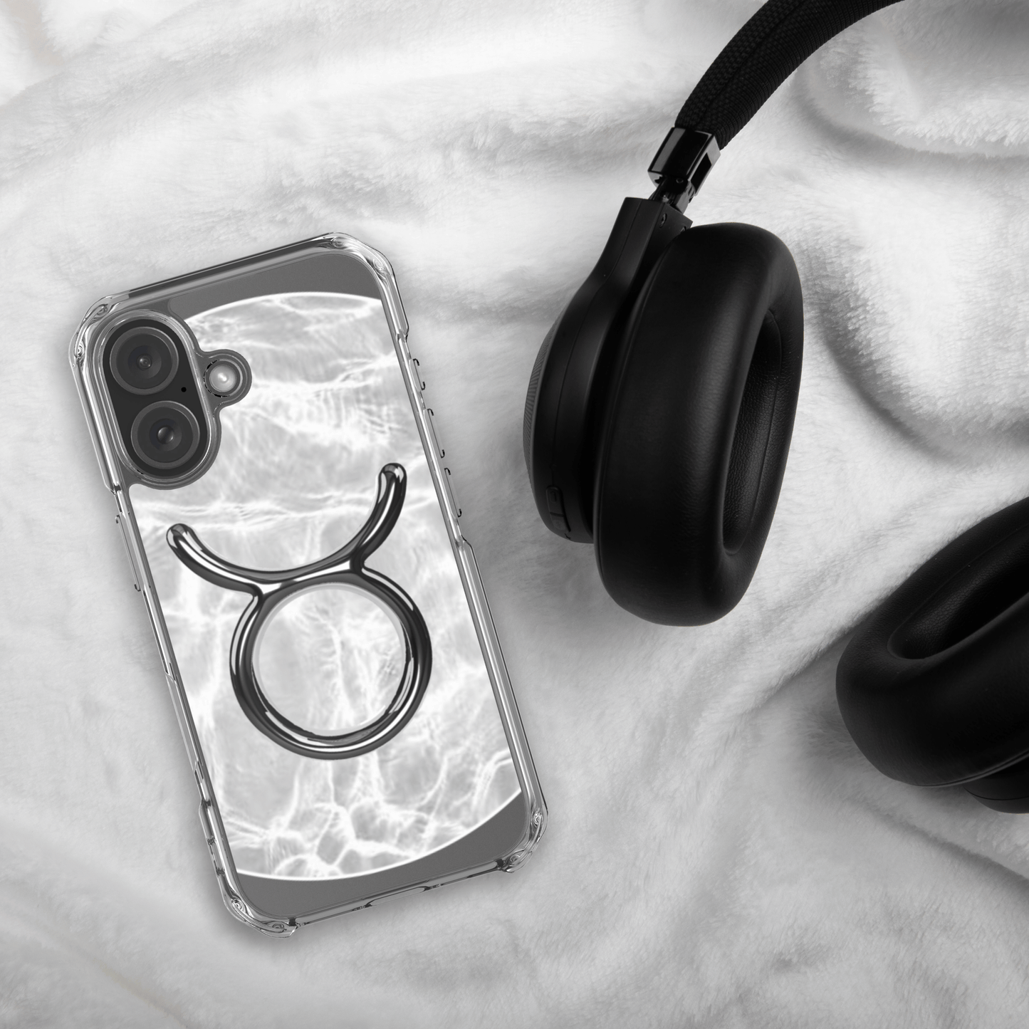 Zodiac Taurus MagSafe clear iPhone case with metallic design on a soft background next to black headphones.