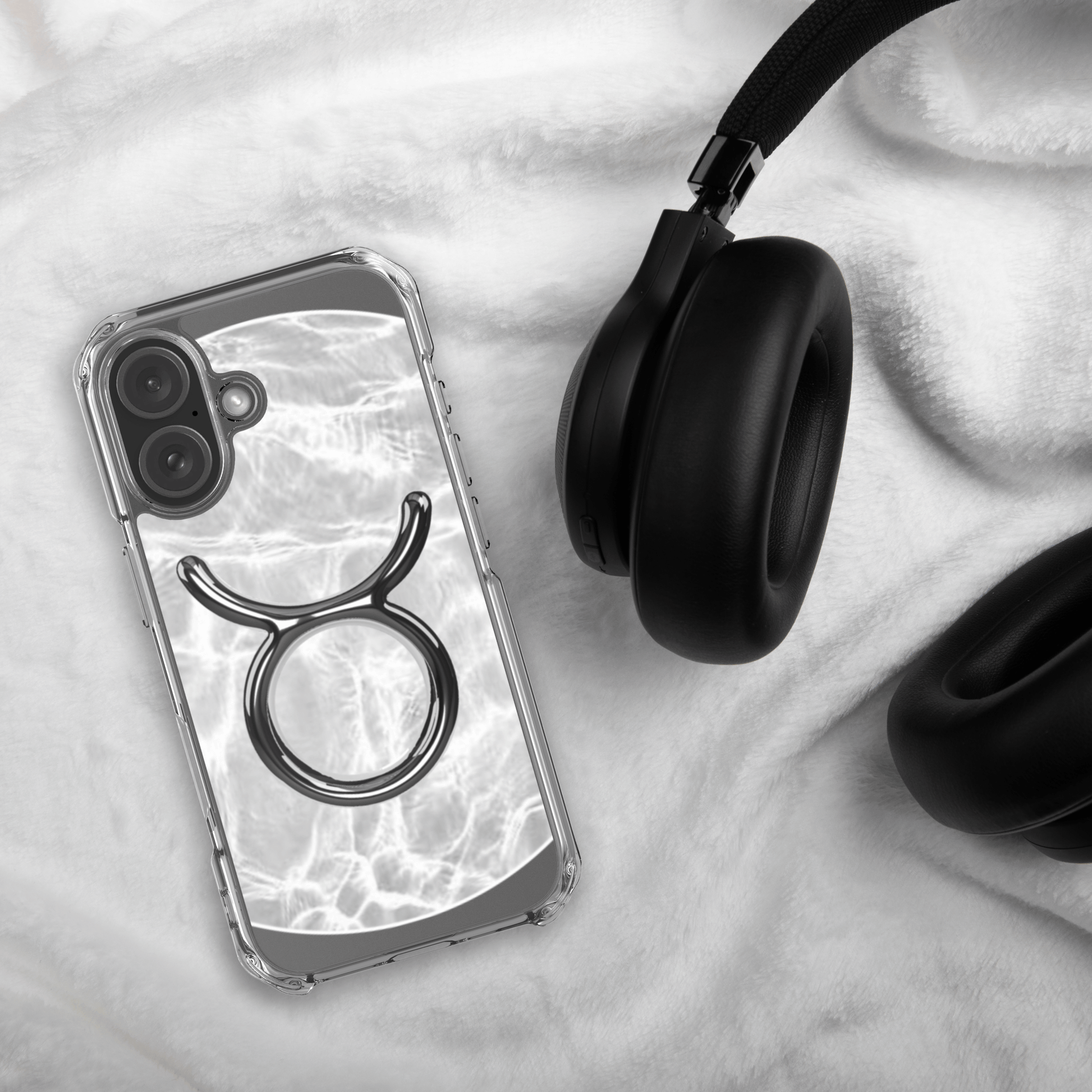 Zodiac Taurus MagSafe clear iPhone case with metallic design on a soft background next to black headphones.