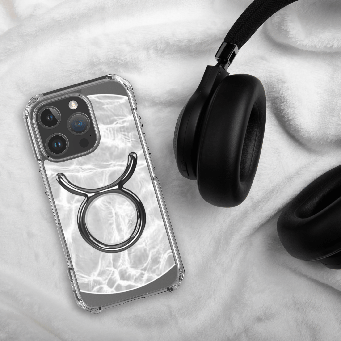 Zodiac Taurus MagSafe clear iPhone case with metallic design, laid beside black headphones on soft fabric.