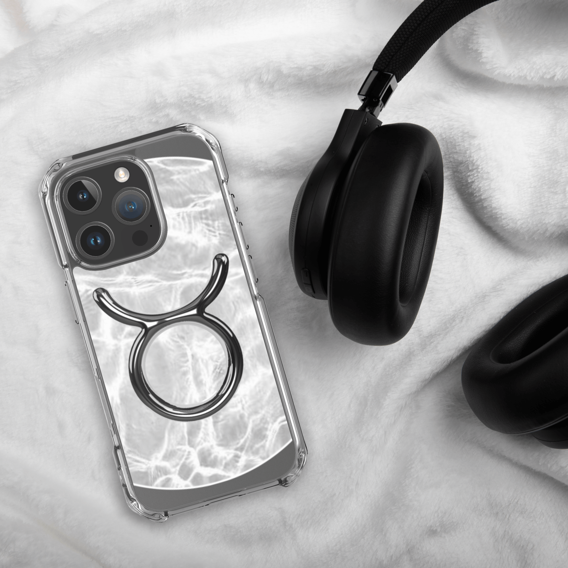 Zodiac Taurus MagSafe clear iPhone case with metallic design, laid beside black headphones on soft fabric.